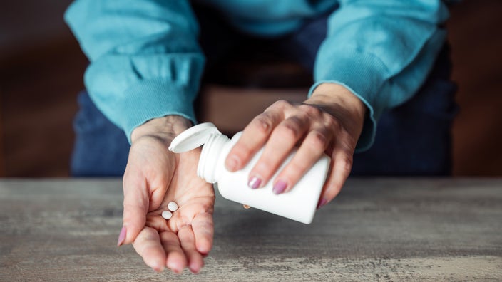 Close-up shot of a woman pouring pills from a bottle into the palm of her hand.