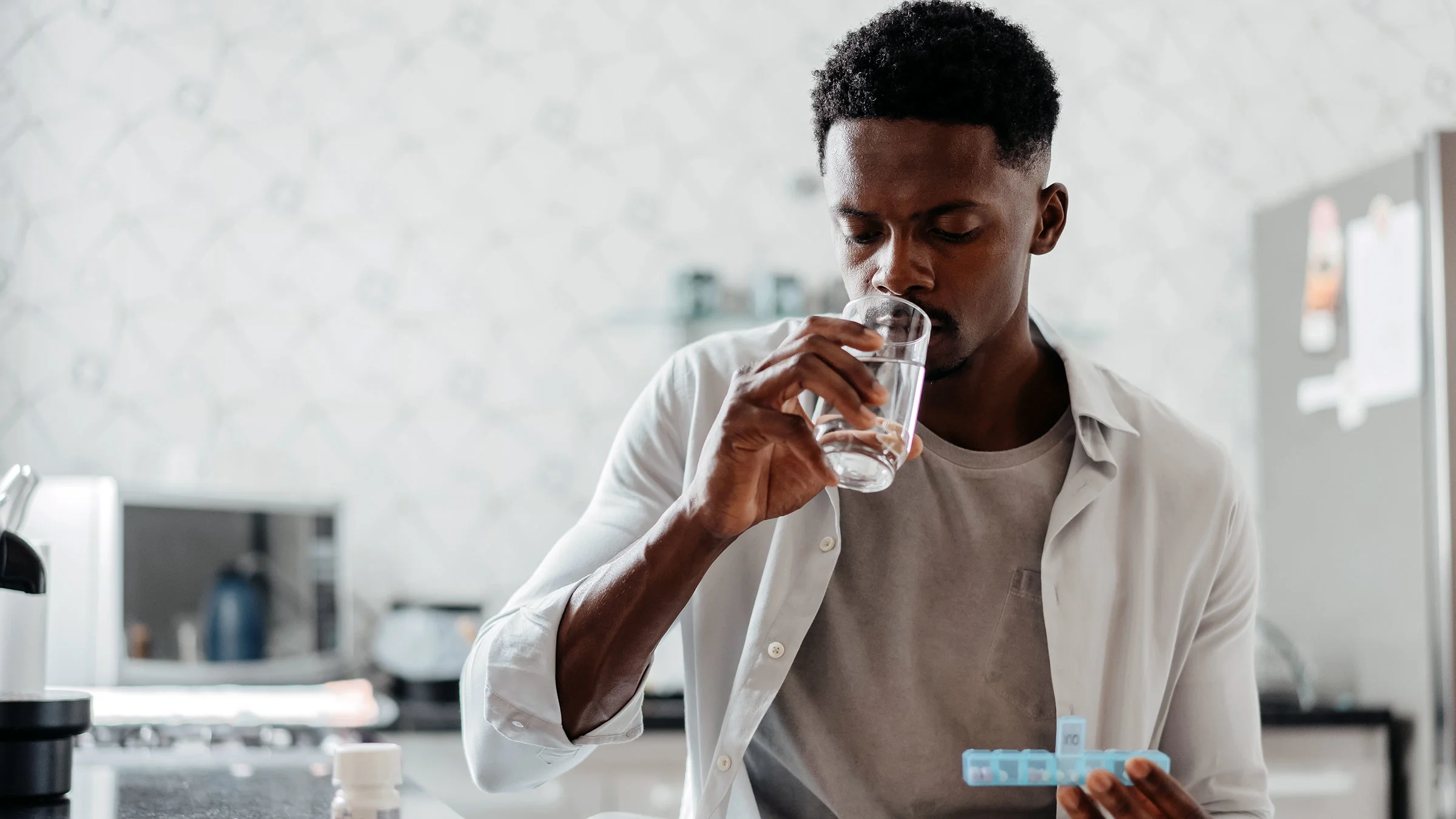 A man takes a drink of water with his medication at home in his kitchen.