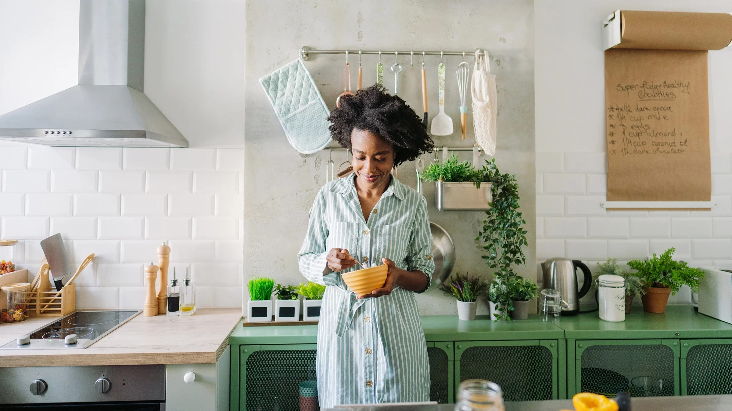 Young woman eating her breakfast in a yellow bowl in her beautiful green and white kitchen.