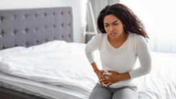 Woman sitting on the edge of the bed grabbing her side in pain.
Prostock-Studio/iStock via Getty Images
