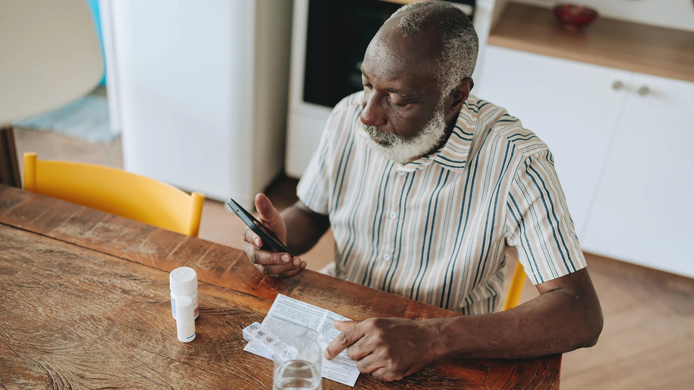 An older man takes his medication at home while checking information on his cellphone. 
andreswd/E+ via Getty Images