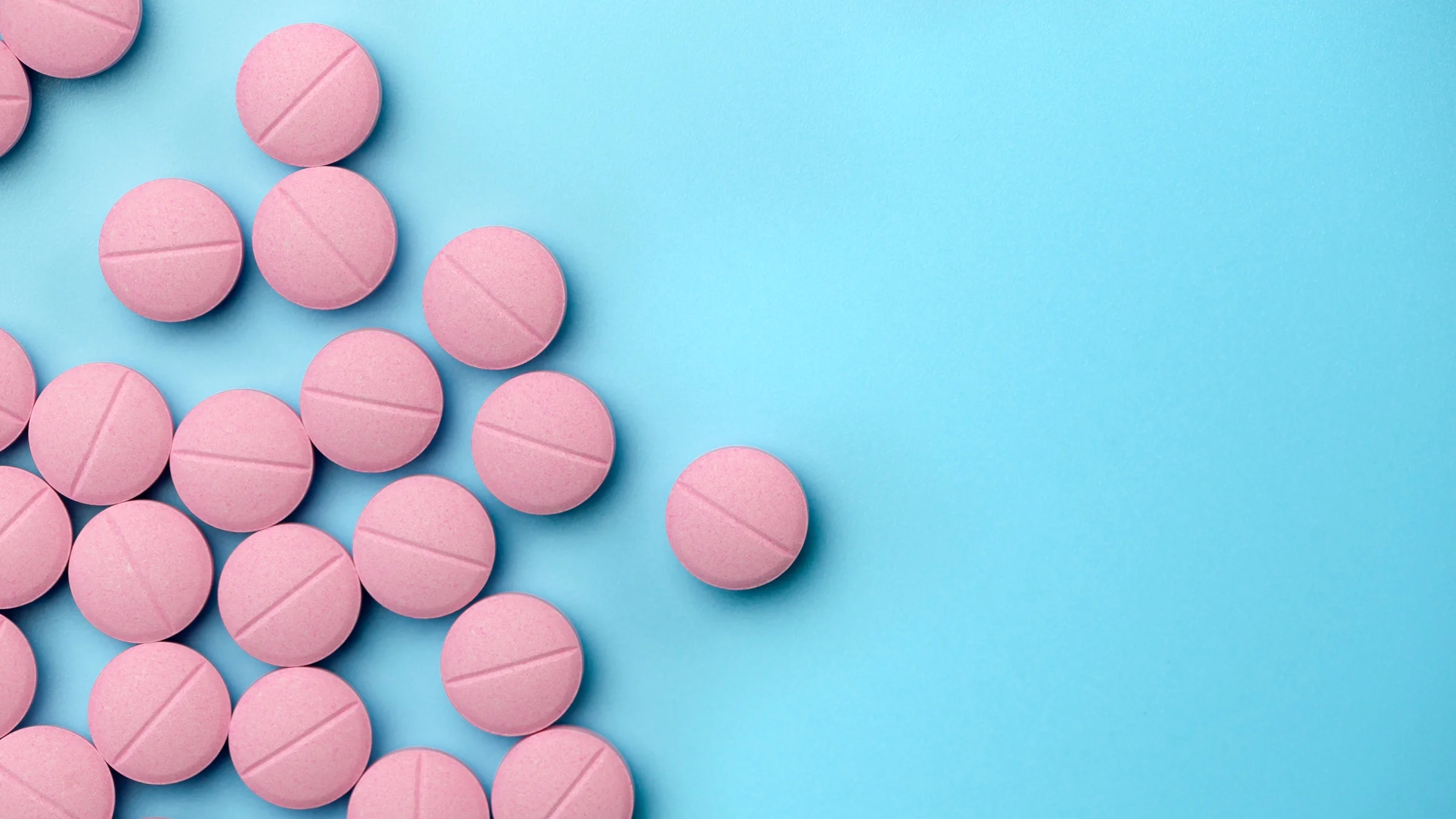 Photo of spilled pink pills against a blue background.