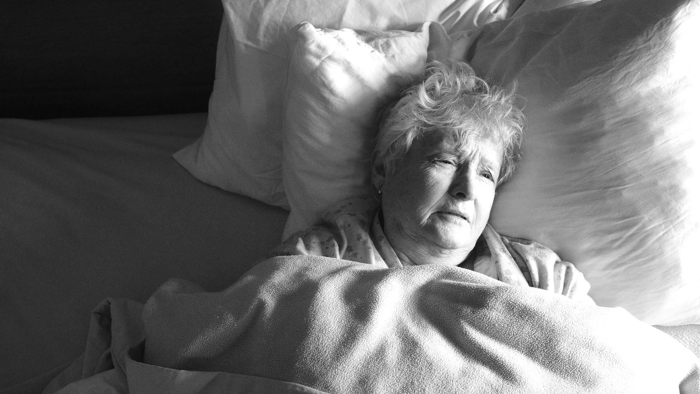 Overhead shot of an elderly woman laying in bed. She looks to be in sad distress.