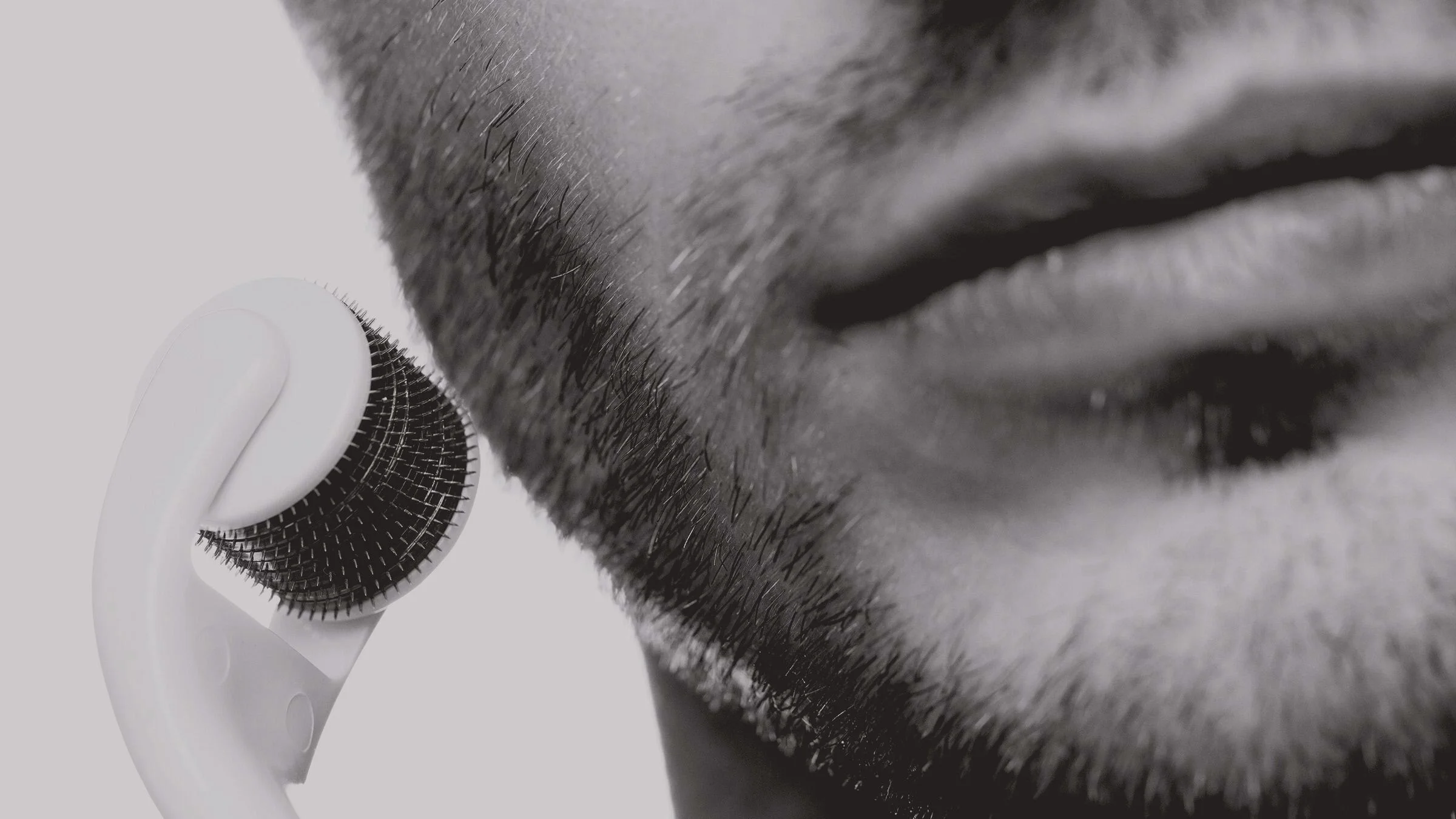 Black-and-white close-up on a man using a micro needle roller on his chin and face.
