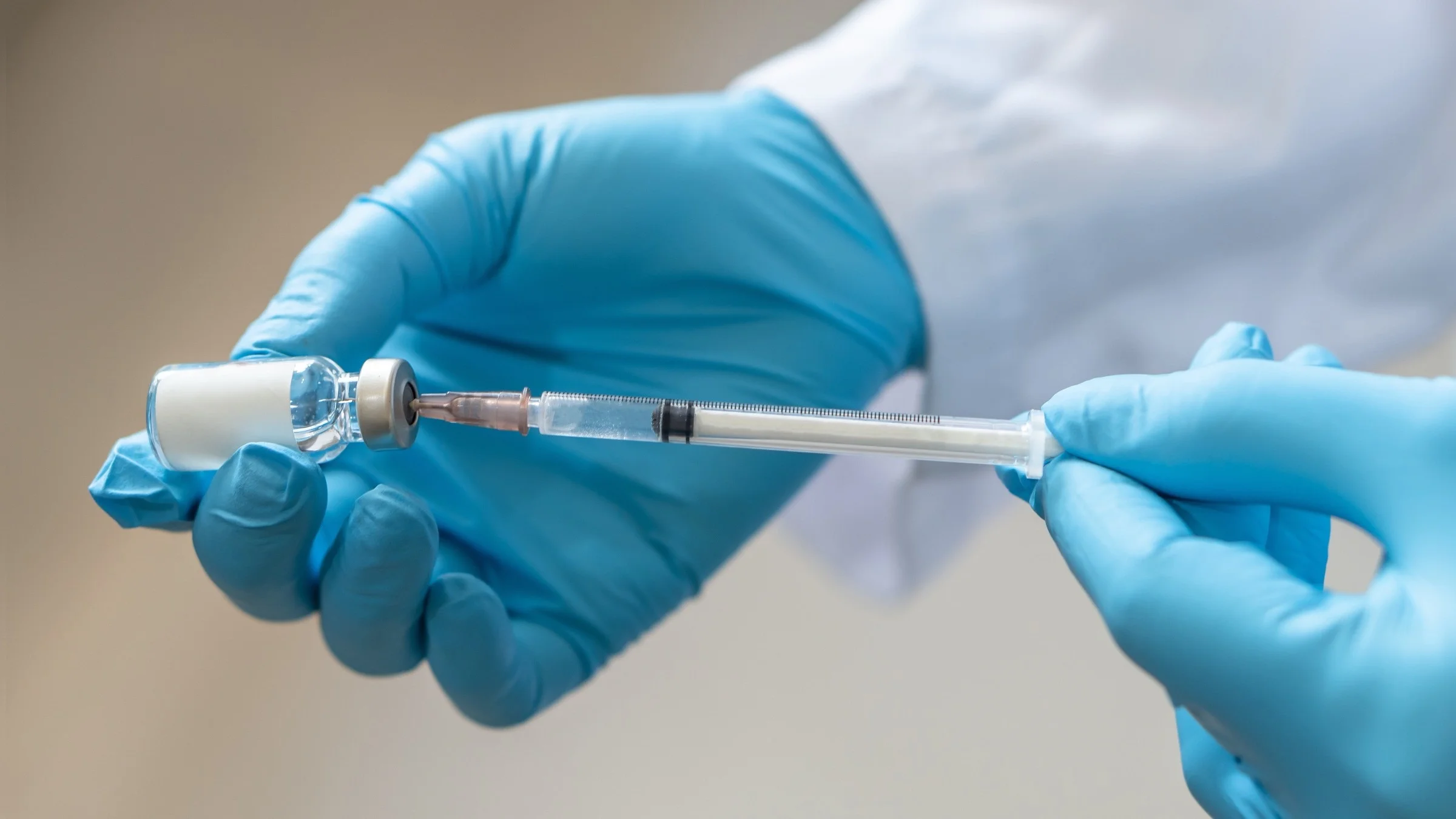 A healthcare provider inserts a syringe into a vial of medication.