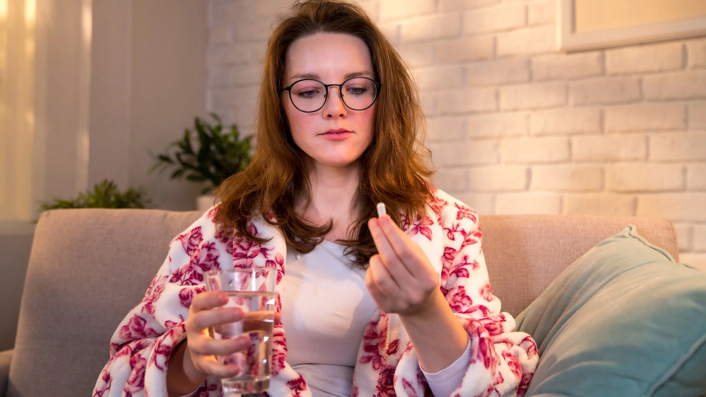 A person taking a pill with a glass of water on their couch.