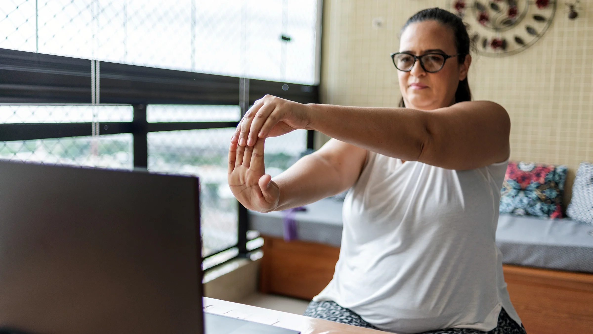 A woman is doing wrist exercises during a telehealth session with a physical therapist.
