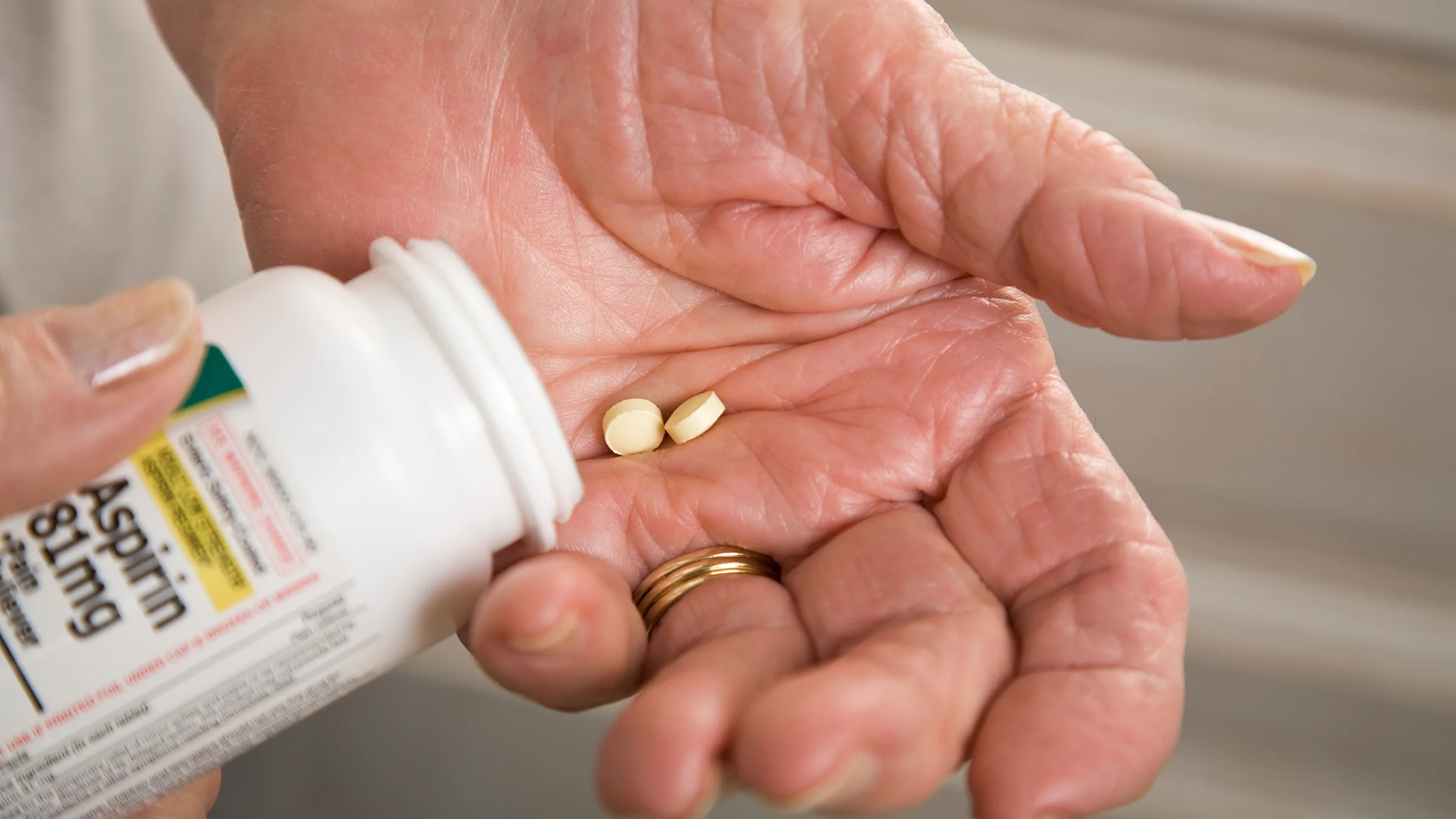 Close-up of a senior person's hands pouring aspirin into their hand.