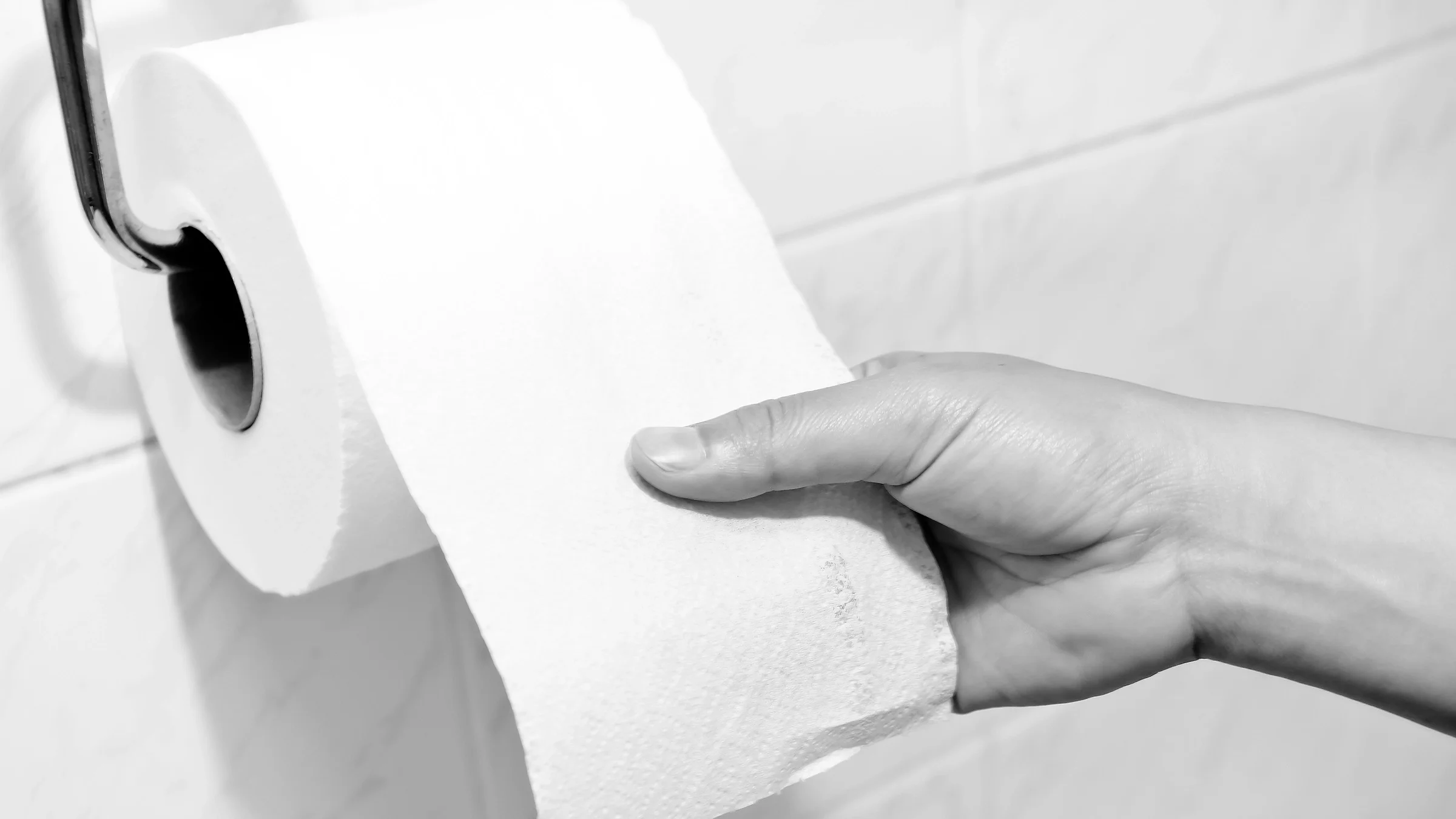 Black-and-white image of a person reaching for toilet paper on the roll.