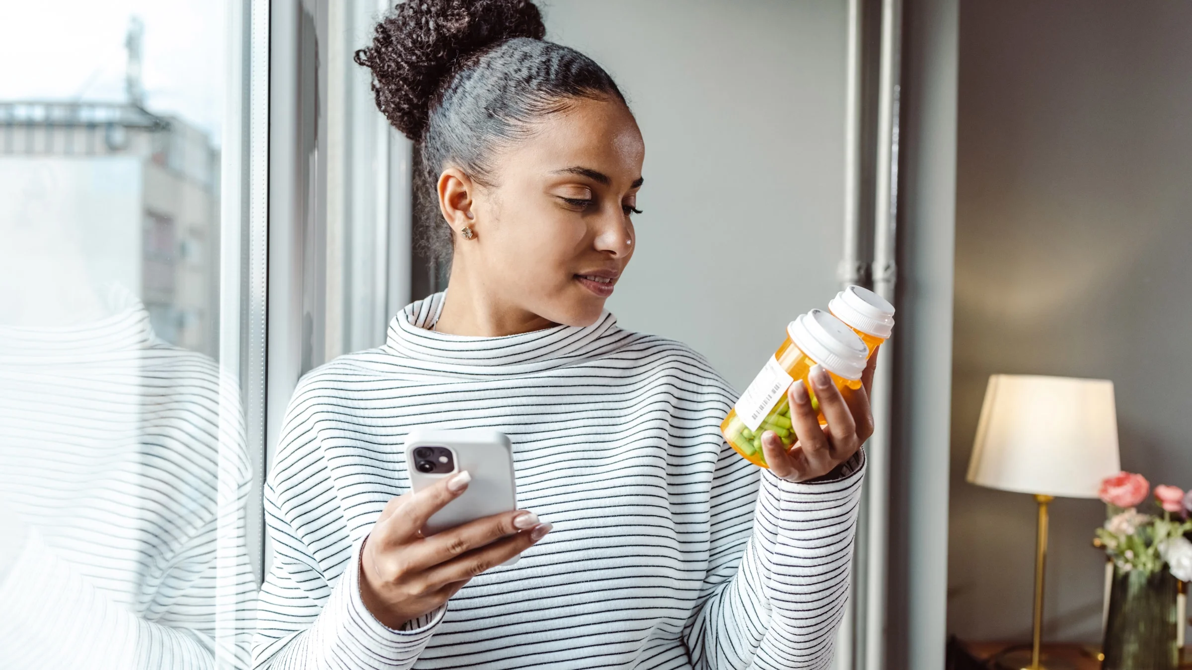 A person holding 2 pill bottles and researching them on their phone.