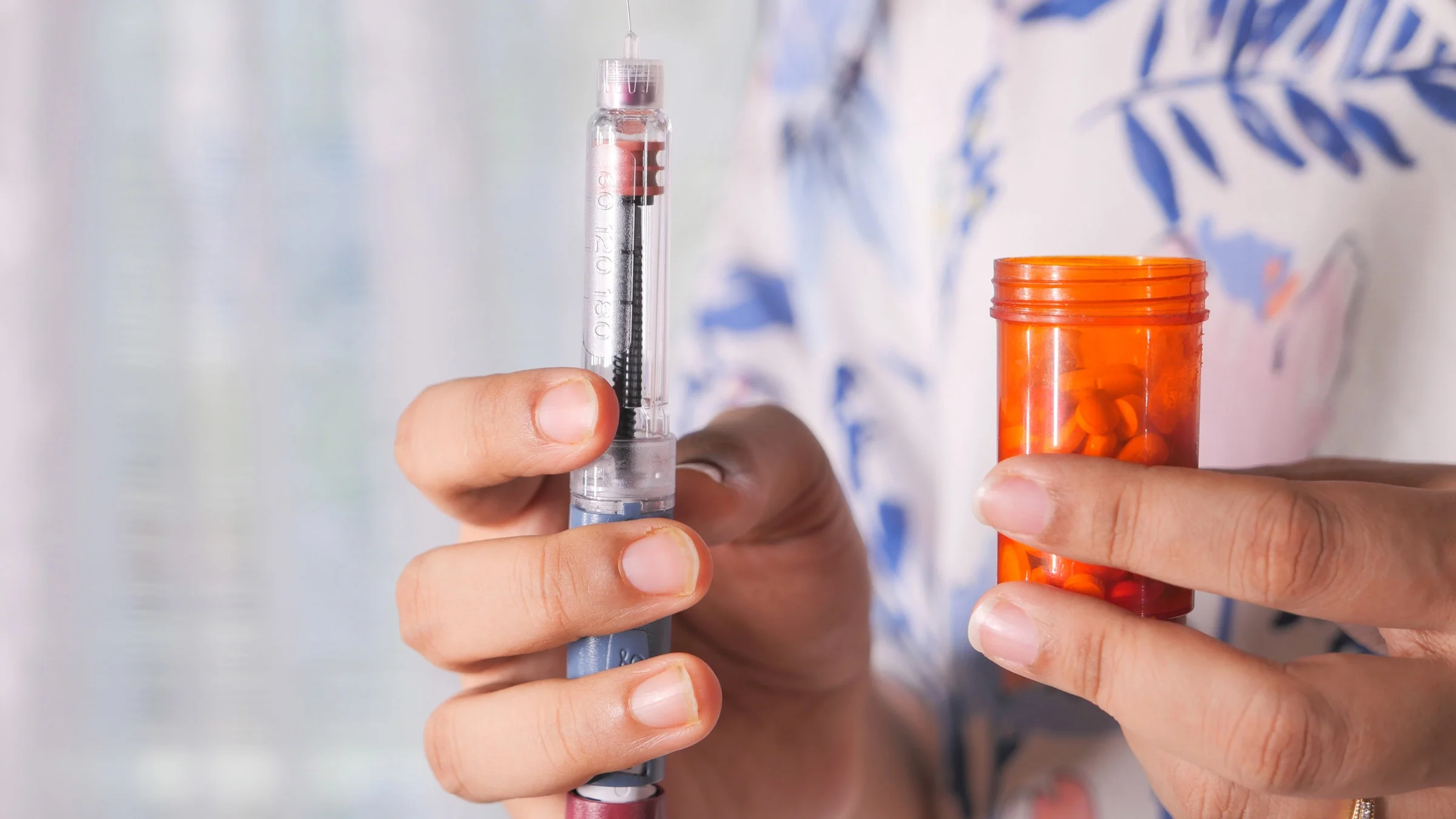 Someone holding an insulin pen and a pill bottle.