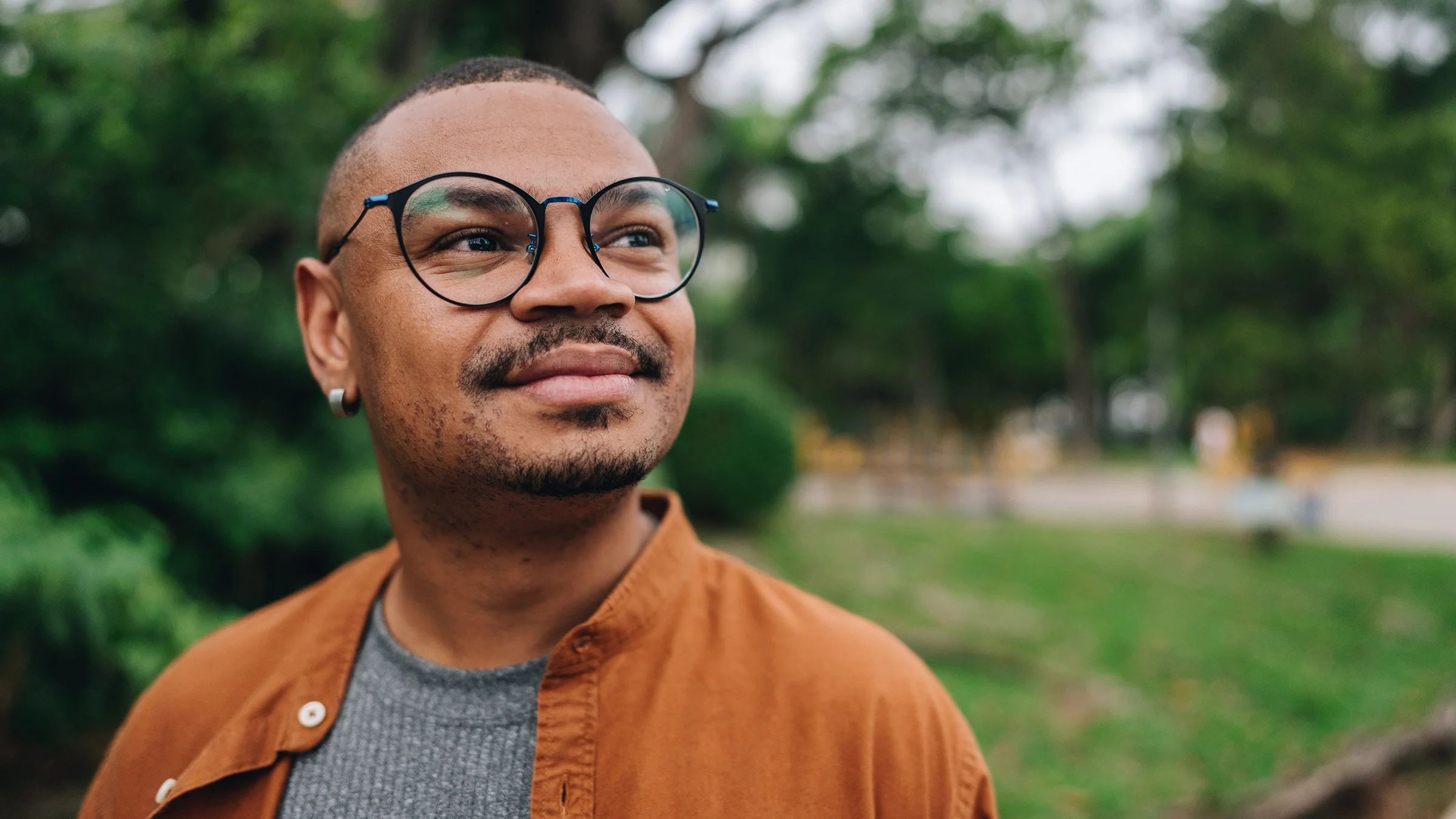 A man wearing glasses is pictured smiling while looking into the distance.