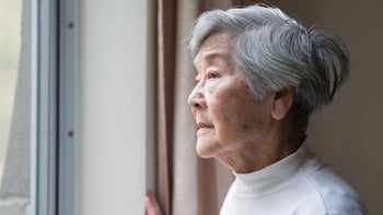 older person staring out window 1296945064