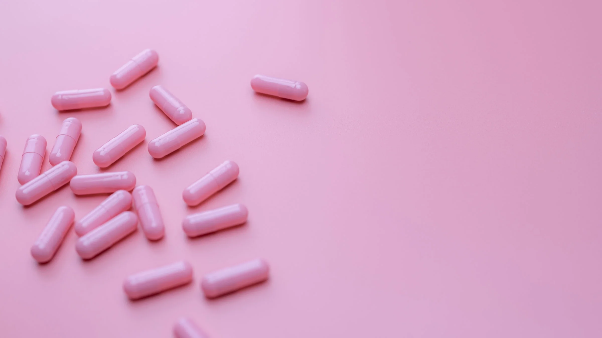 Still life of pink capsule pills on pink background.