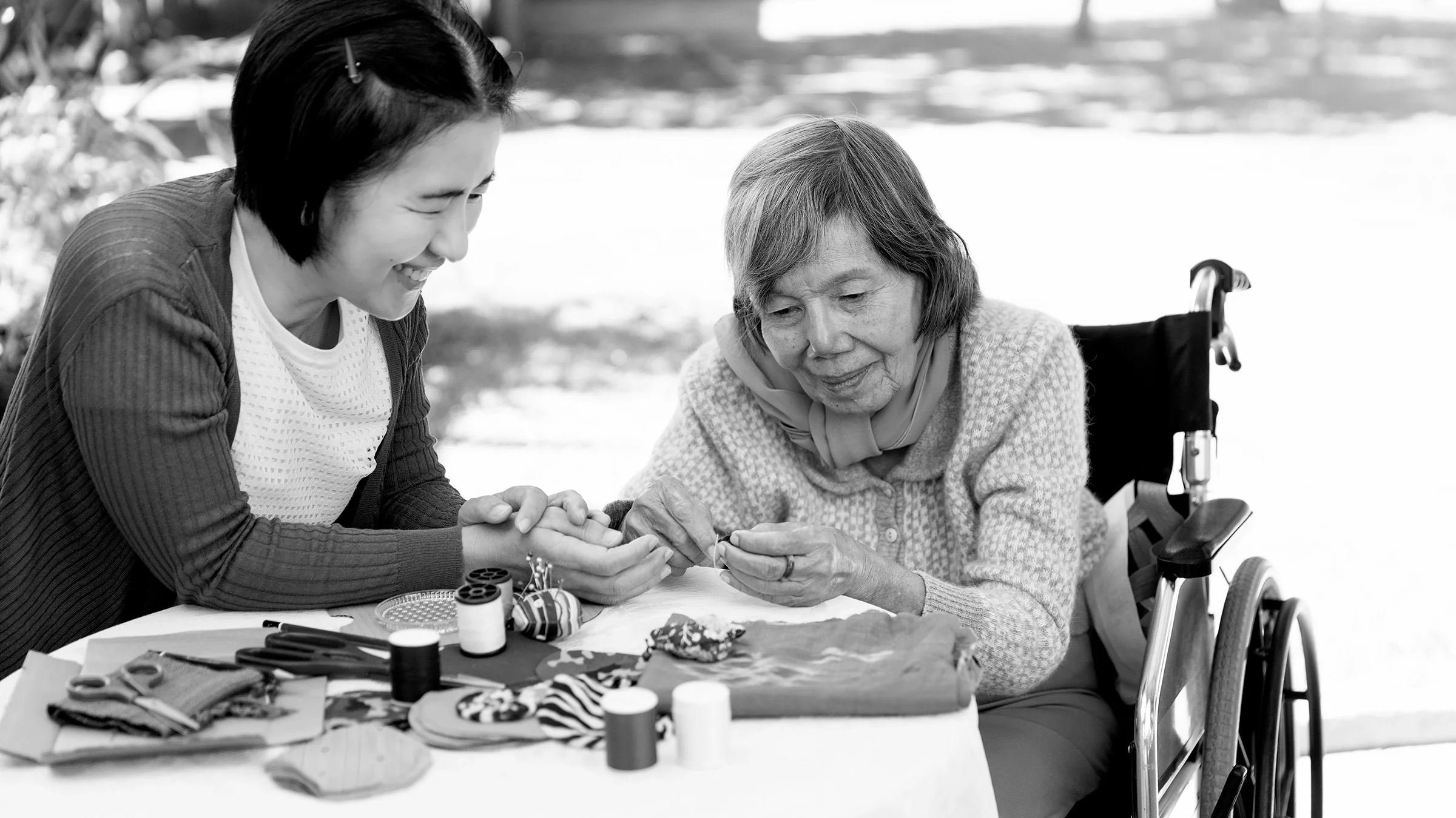 Black and white image of a daughter doing art therapy with her mother with dementia. They are outside.
