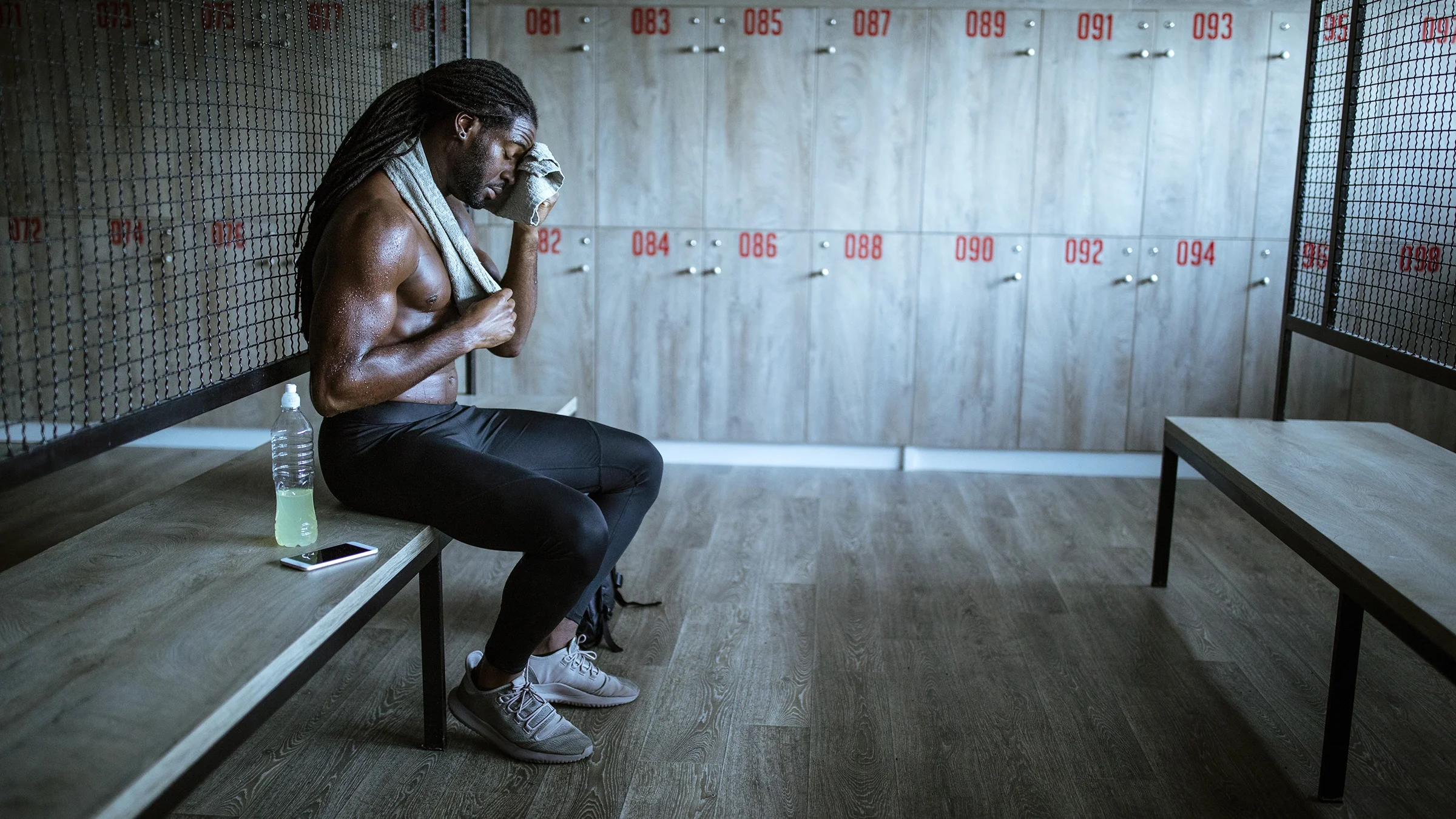 A man wipes sweat from his brow post-workout in a locker room.