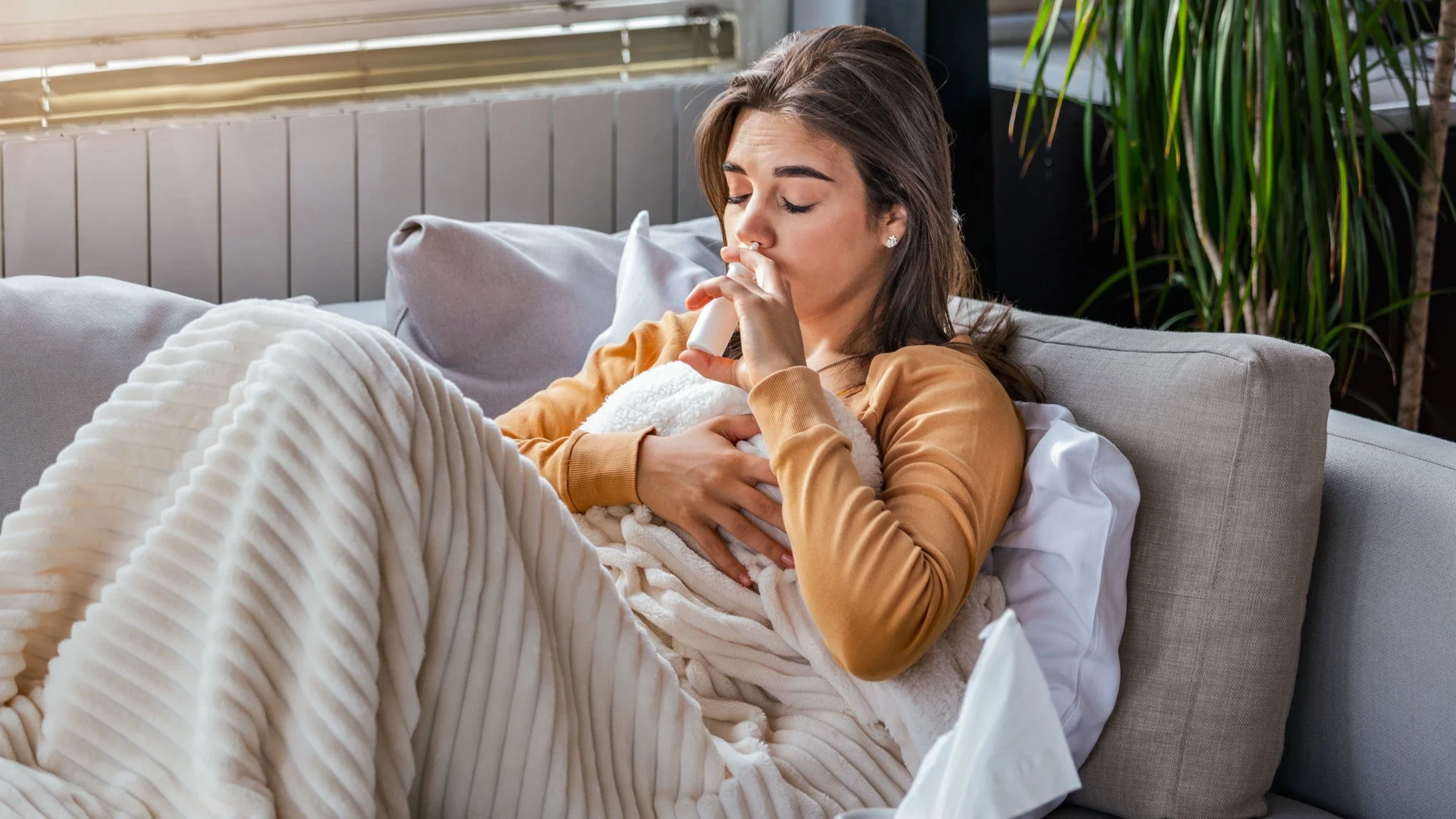 A person sitting on their couch using a nasal spray.