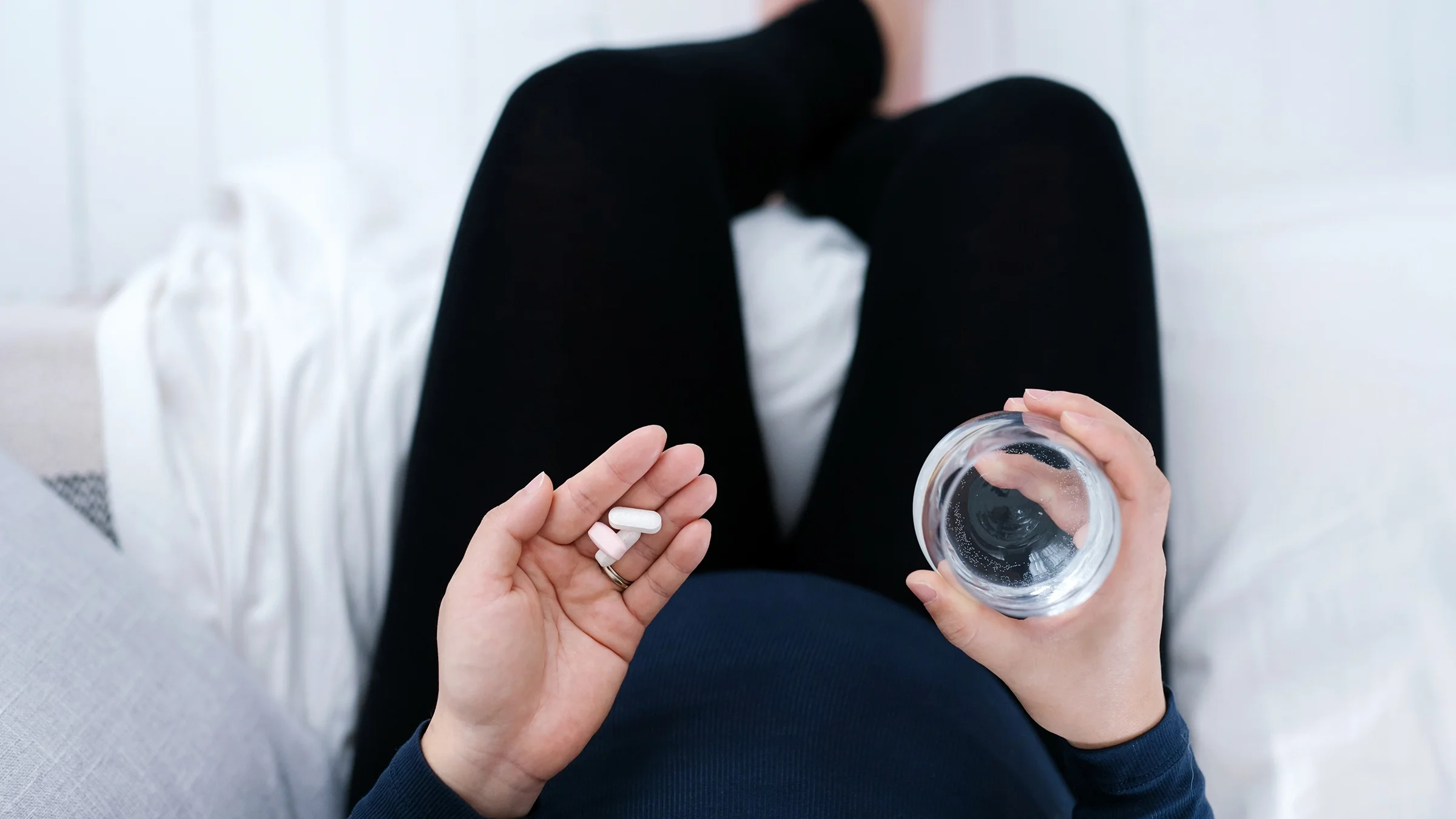 A top-down view of a woman taking medication with a glass of water.