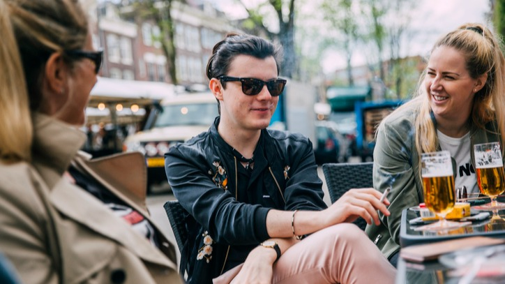 Group of friends having beer outside at a restaurant while the smoke cigarettes.