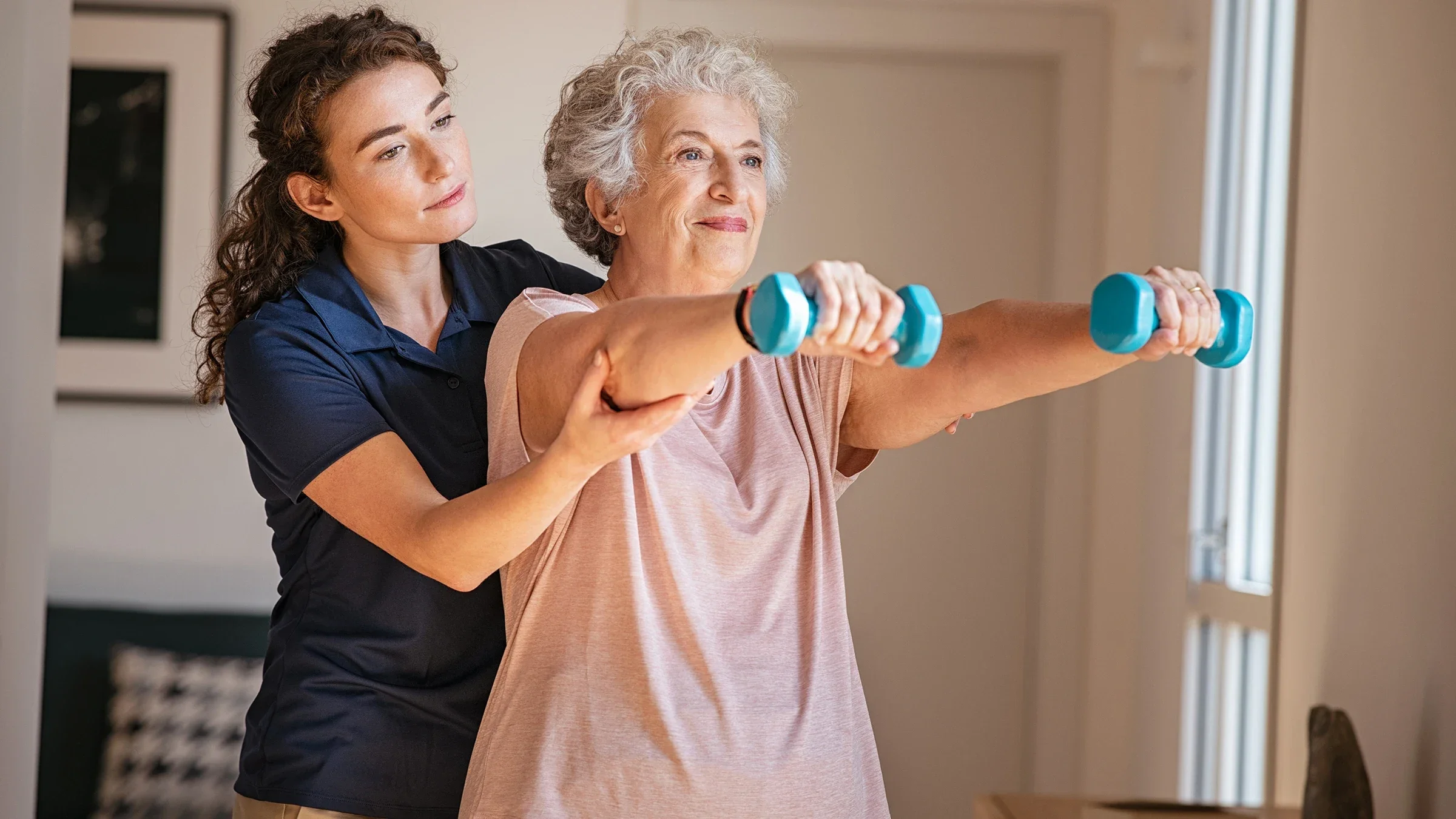 Senior woman lifting weights while doing physical therapy with a nurse at home.
Ridofranz/iStock via Getty Images