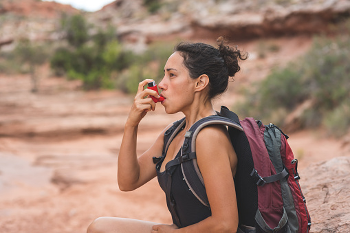 Young woman using an inhaler outdoors hiking with a backpack.