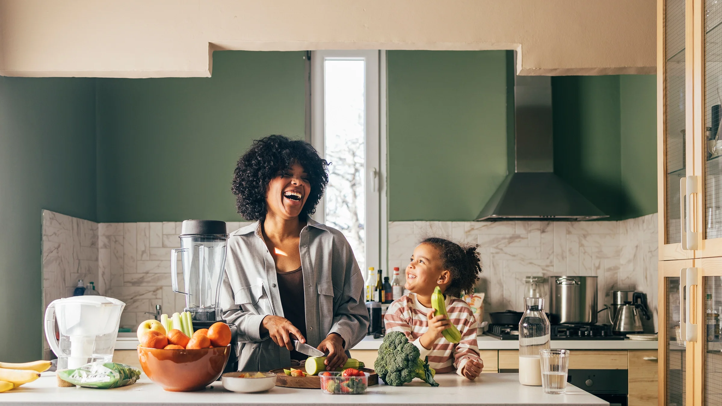 A mother and daughter are smiling while cutting vegetables in the kitchen.