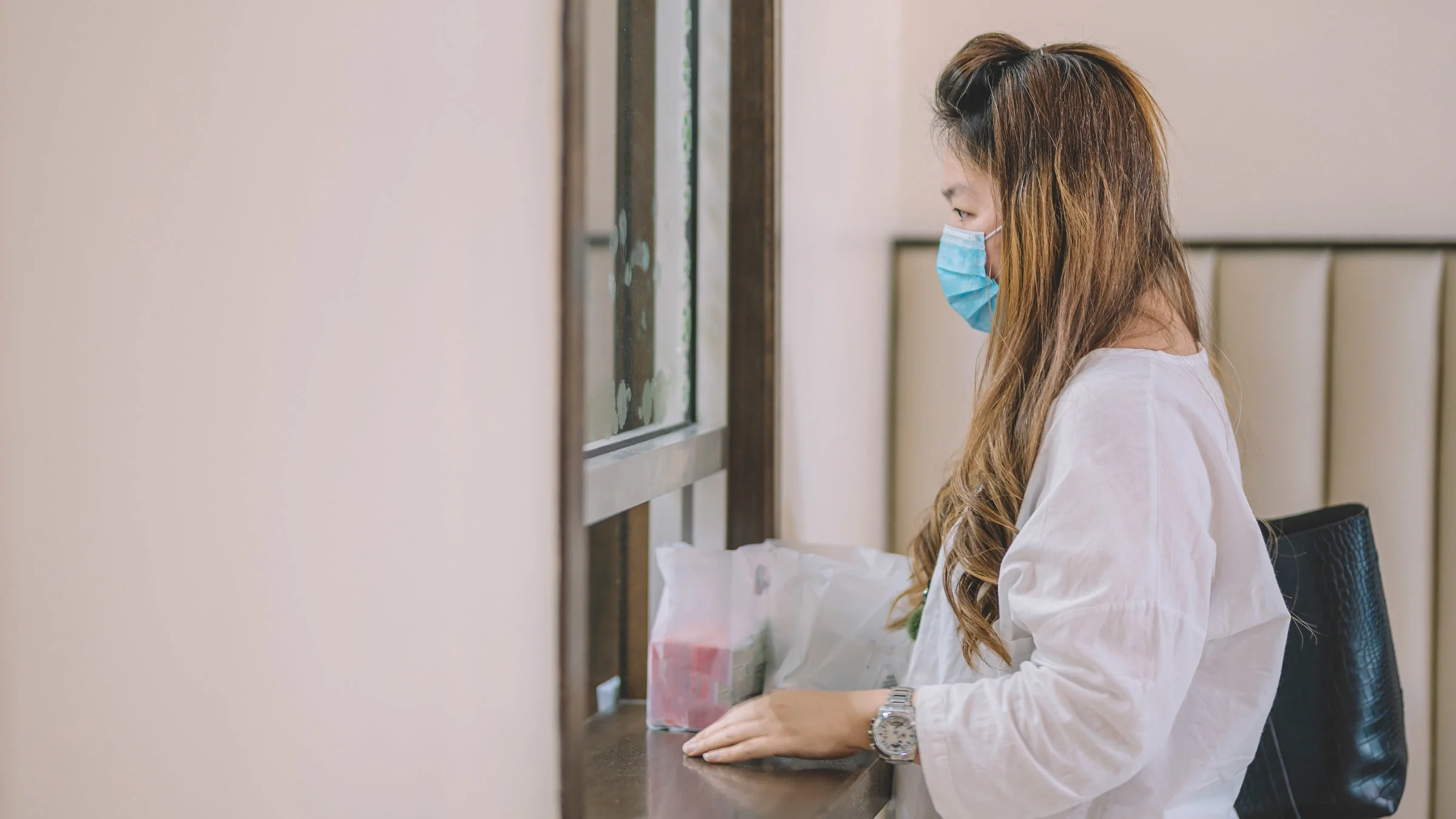 A masked patient picking up their prescription a pharmacy window.