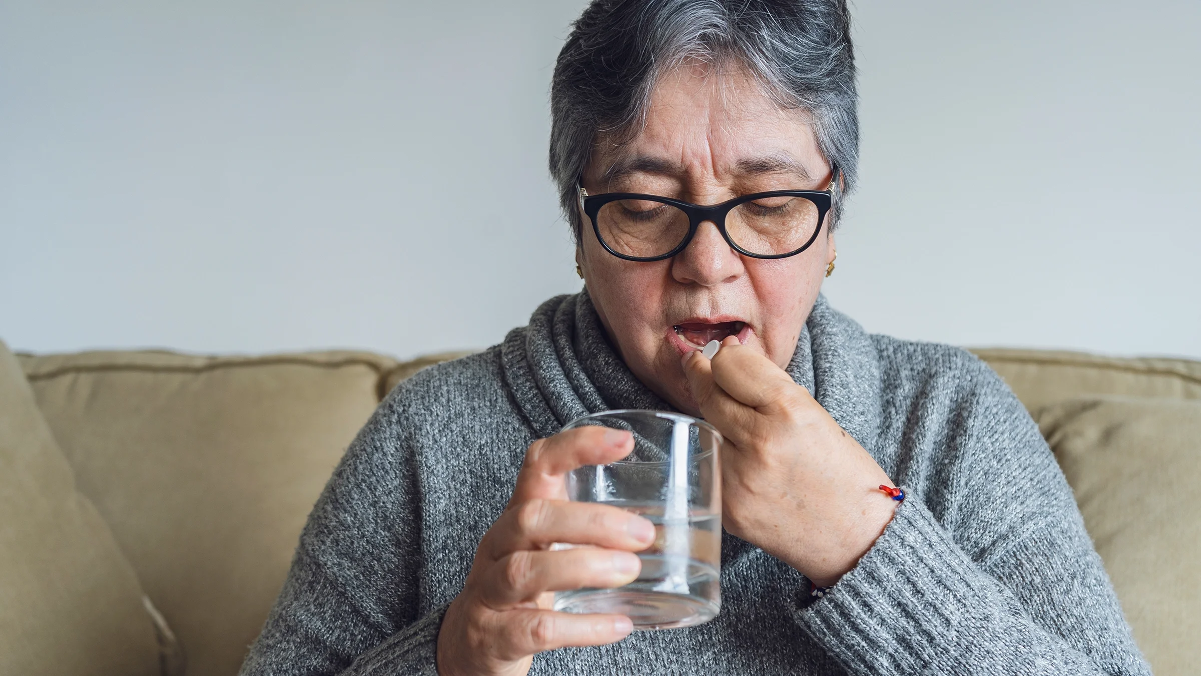 A woman takes a pill at home.