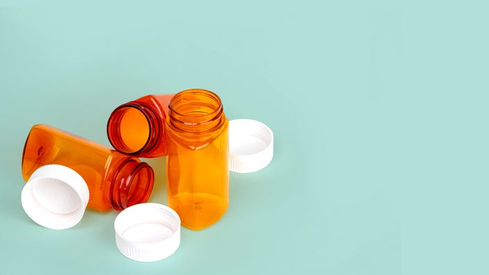 Three empty orange prescription bottles on a light green background. All three are open with their lids laying next to them.