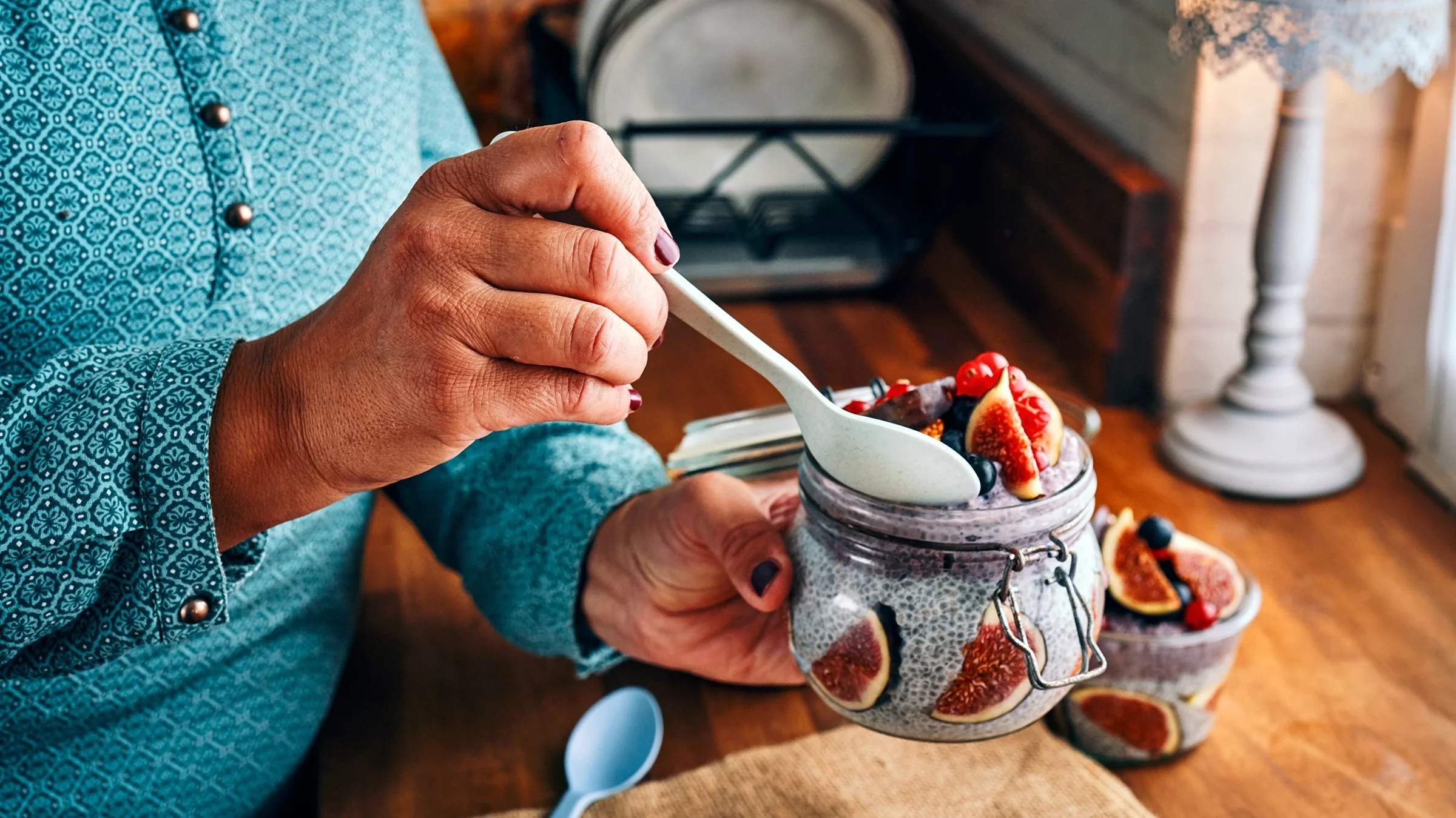 A woman dips a spoon in a chia-seed pudding with fruits, which are some of the foods that can help increase GLP-1. 