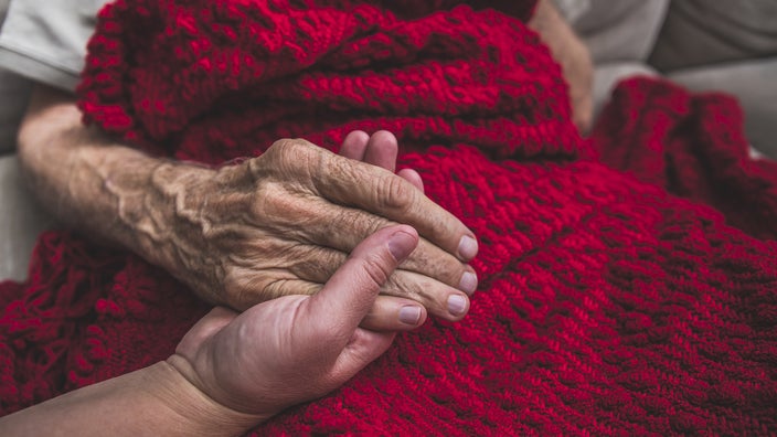 Close-up hand holding with an older adult under a red knit blanket