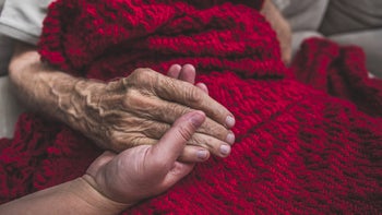 Health: End of life: closeup holding hands under knit blanket 895072326