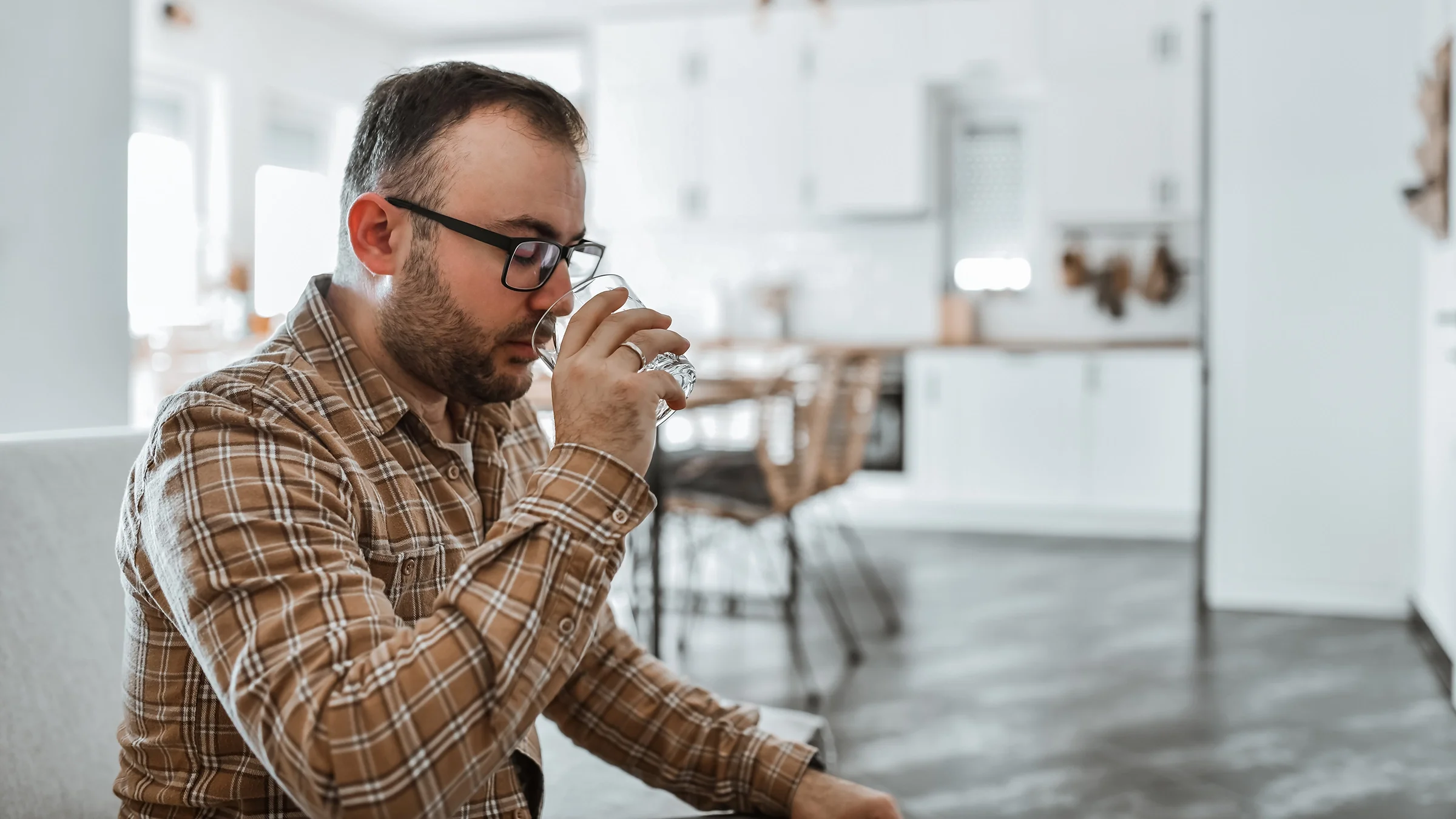 A man drinks from a glass in his home kitchen. 