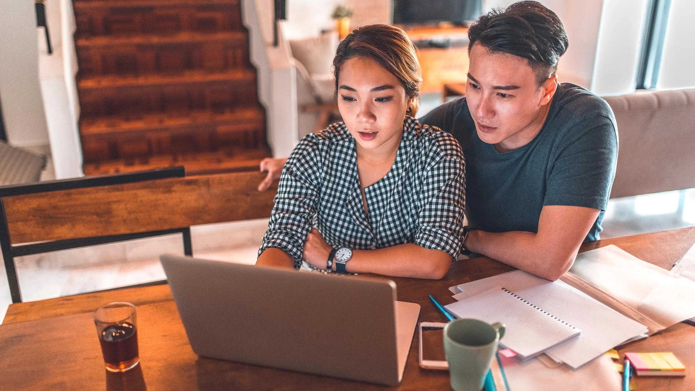 Young couple sitting at their dining table with their laptop and paperwork and notes surrounding them.