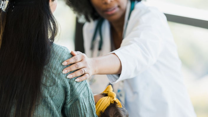A doctor consoles a new mom while carrying a baby.