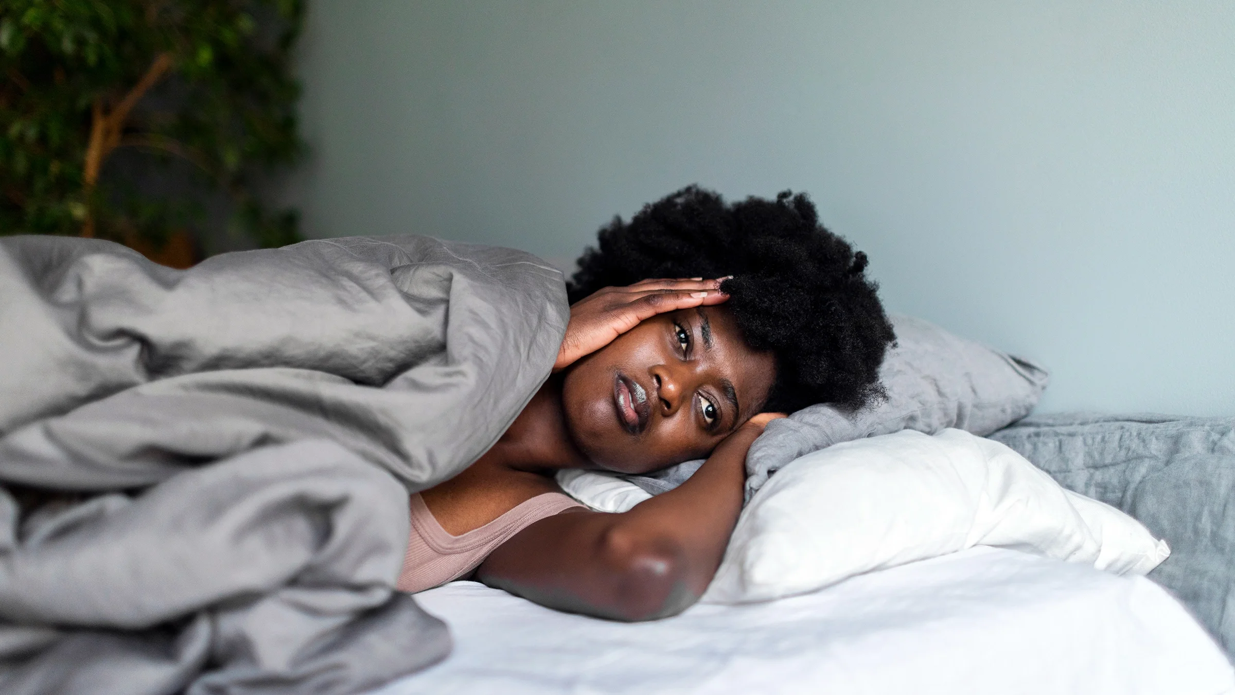 A woman who appears to be sad lies in bed.