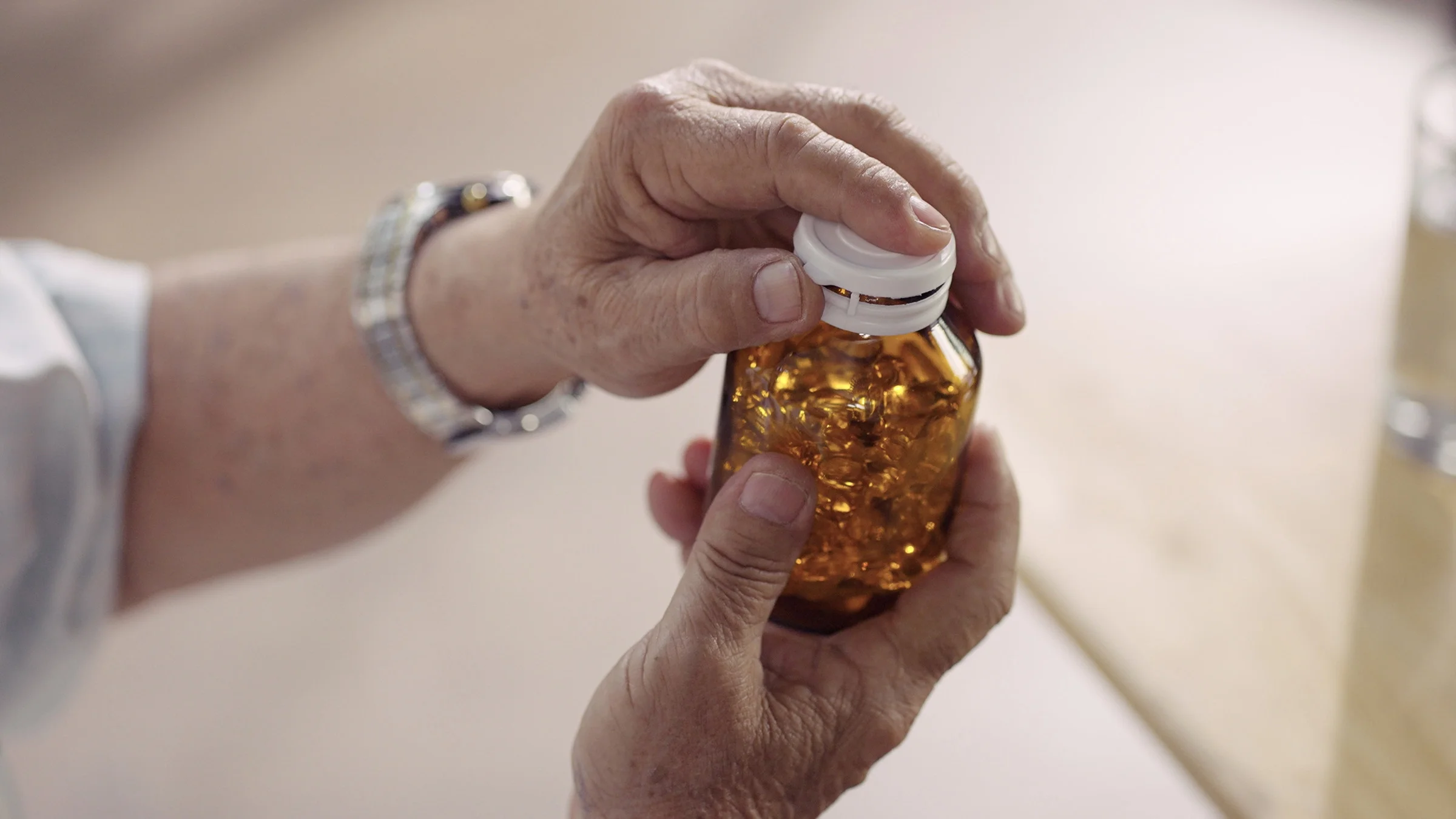 Close-up of an elderly man's hands opening a glass bottle of supplements.