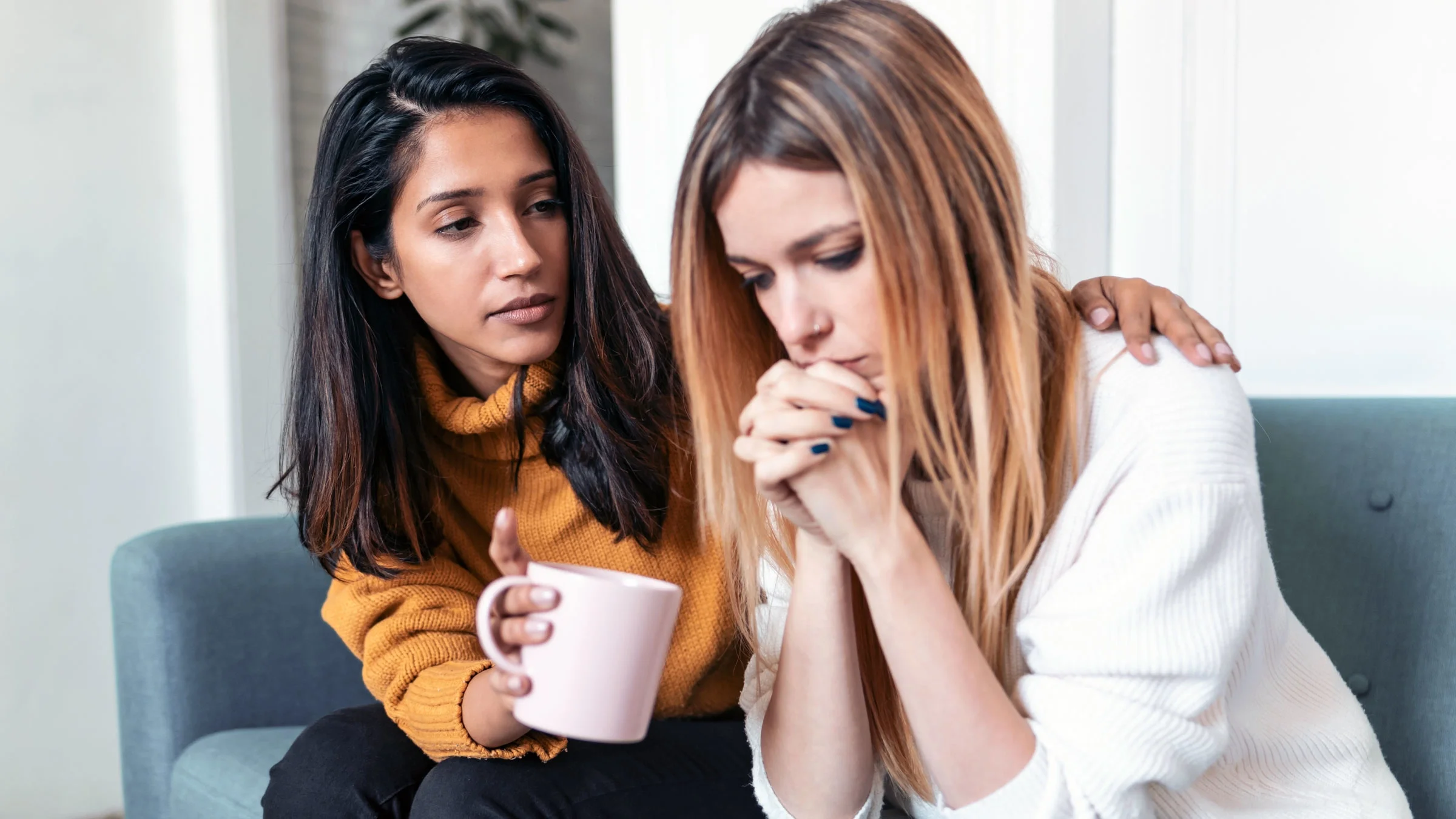 Woman comforting her sad friend while sitting on the sofa at home.