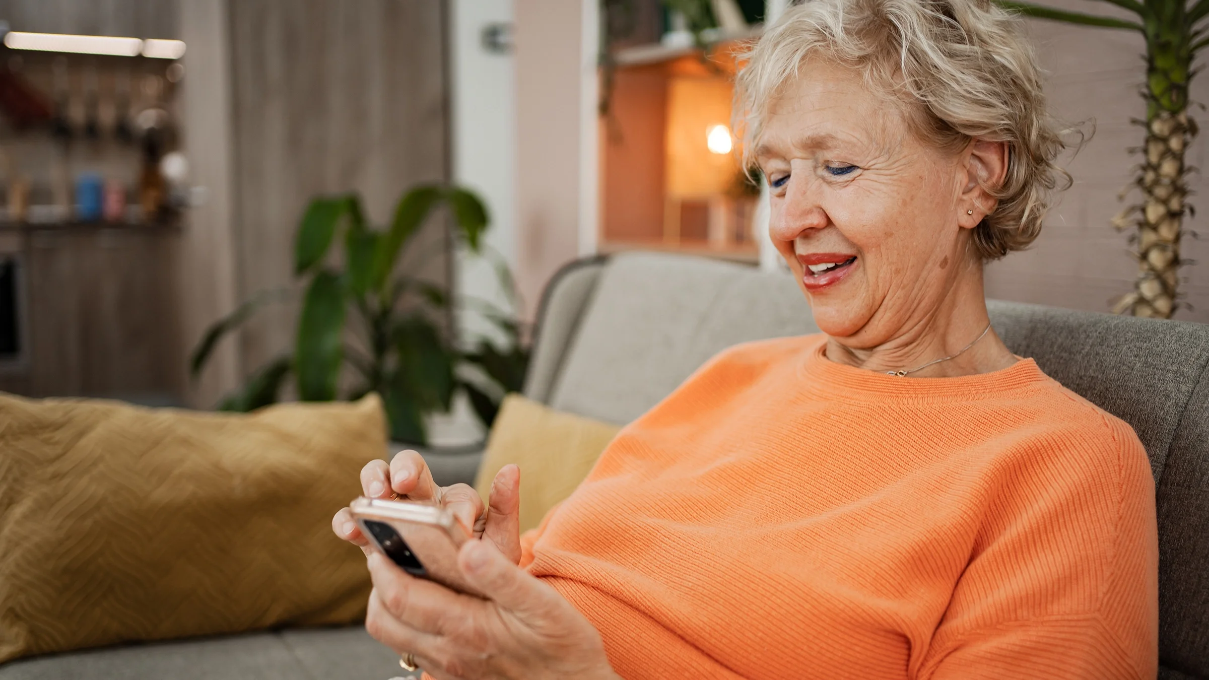 A woman using a smartphone relaxes on a sofa at home.