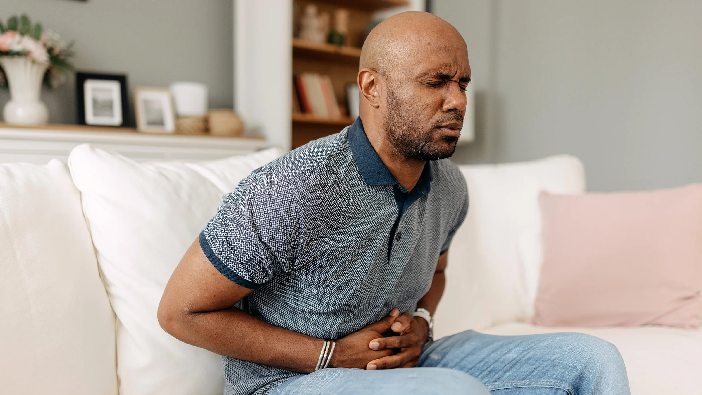Man clutching his stomach in pain on a white sofa.