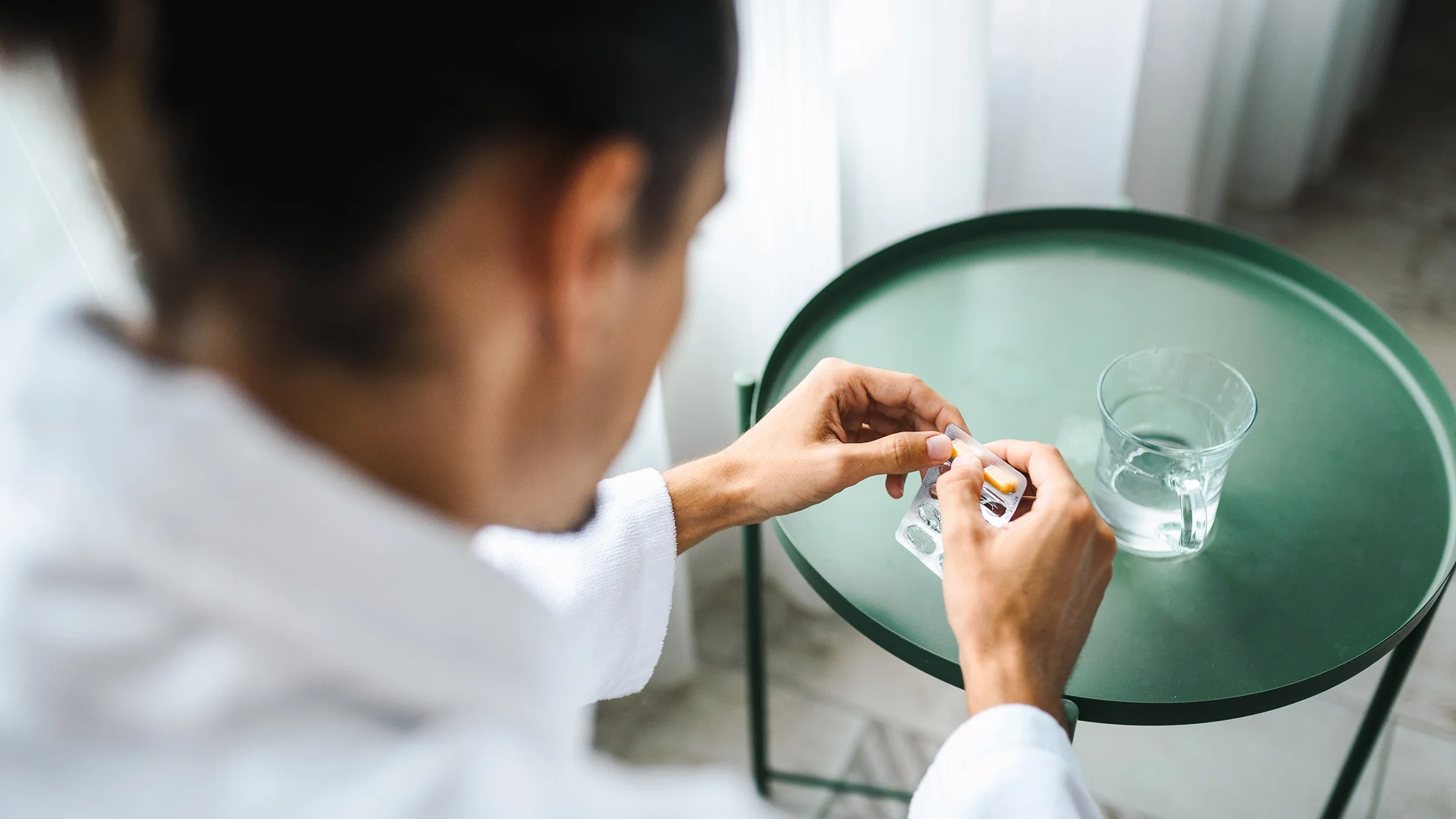 A man, shown in close-up, opens a blister pack of pills.