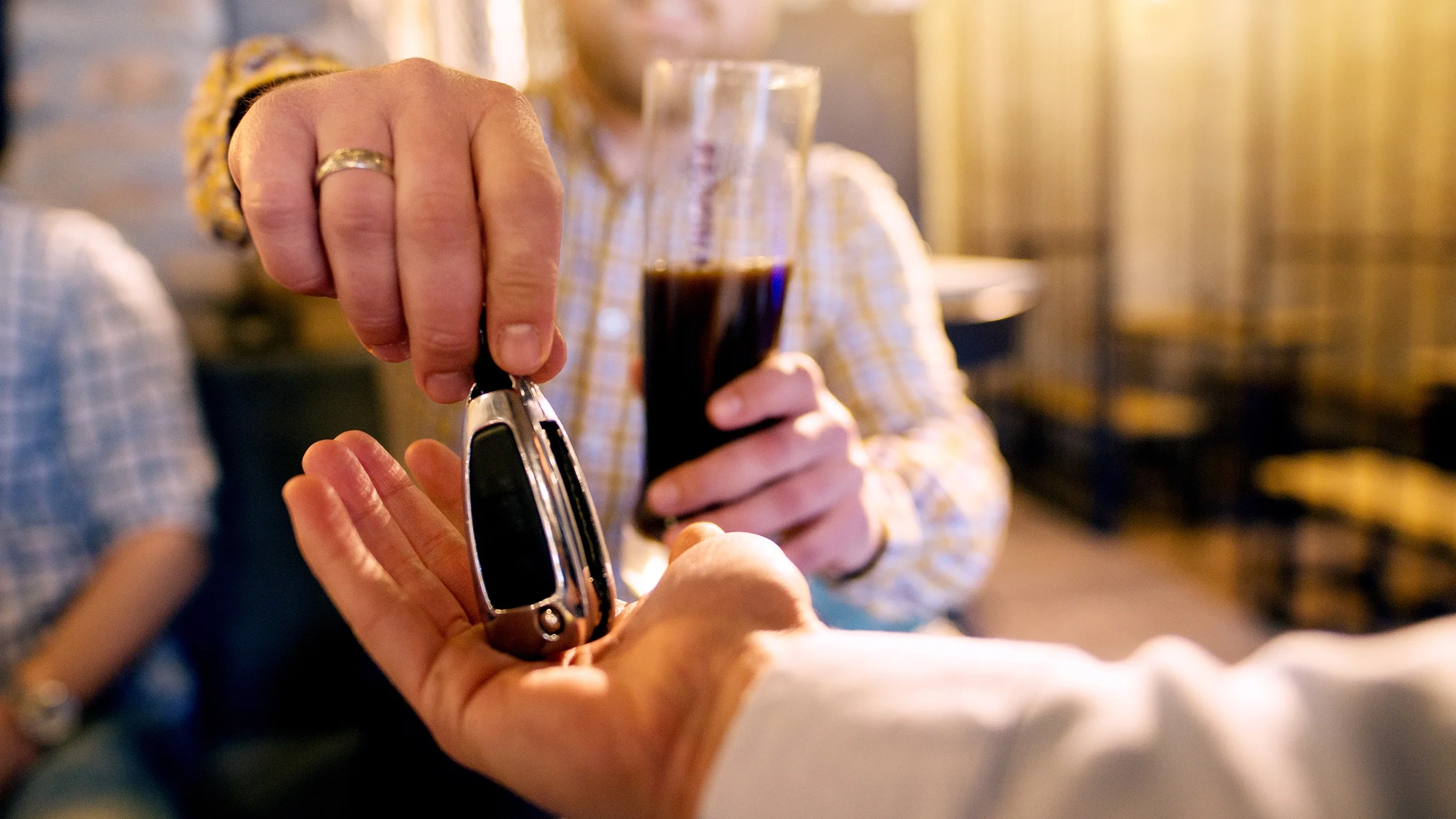 Close-up of a person handing their friend their car keys. They have been drinking and have a beer in their hand.