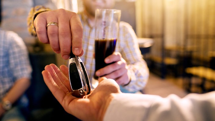 Close-up of a person handing their friend their car keys. They have been drinking and have a beer in their hand.