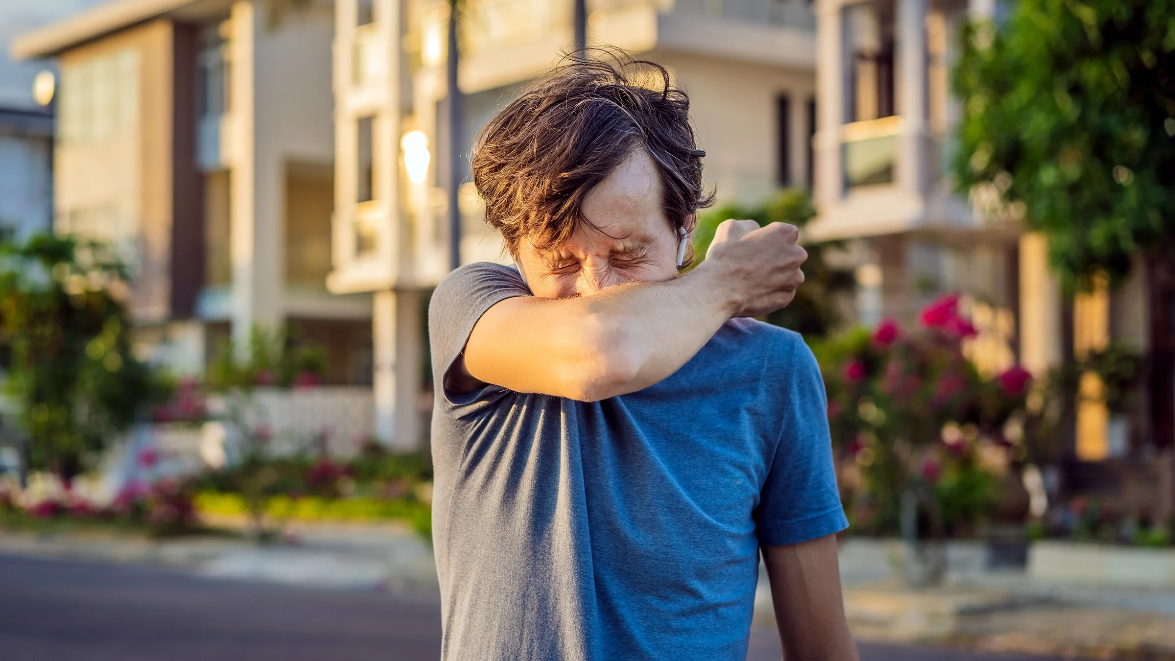 A man sneezes into his elbow while on a walk outside.