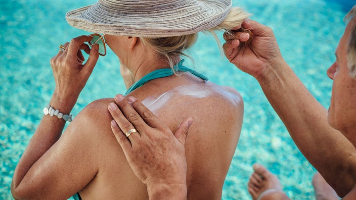 Woman gets sunscreen applied to her back.