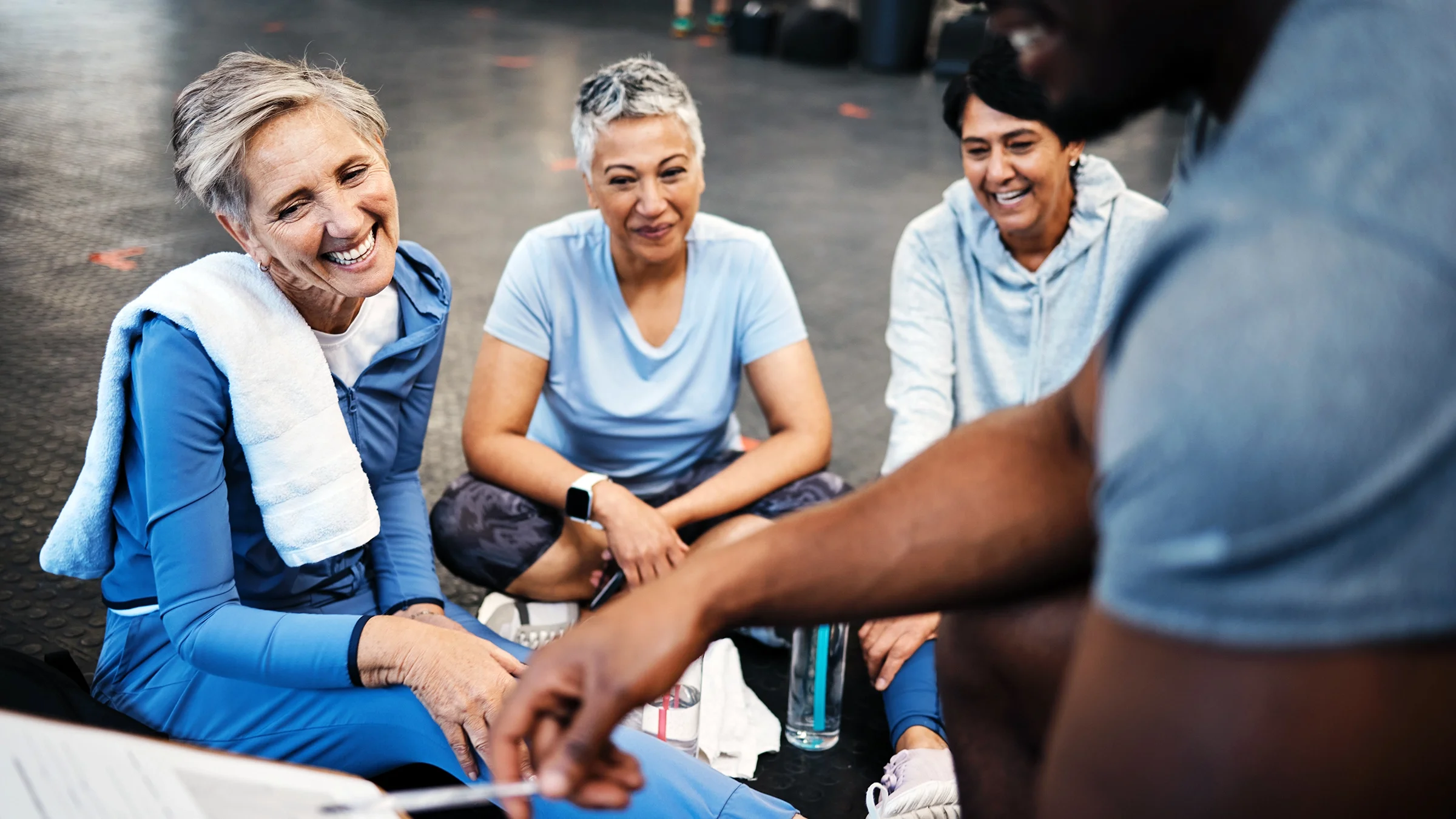Three senior women talk to a trainer at a gym.