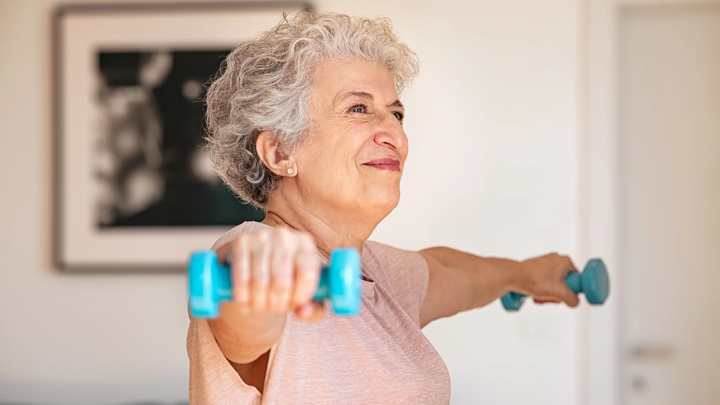 A senior woman does a lateral raise exercise with weights.