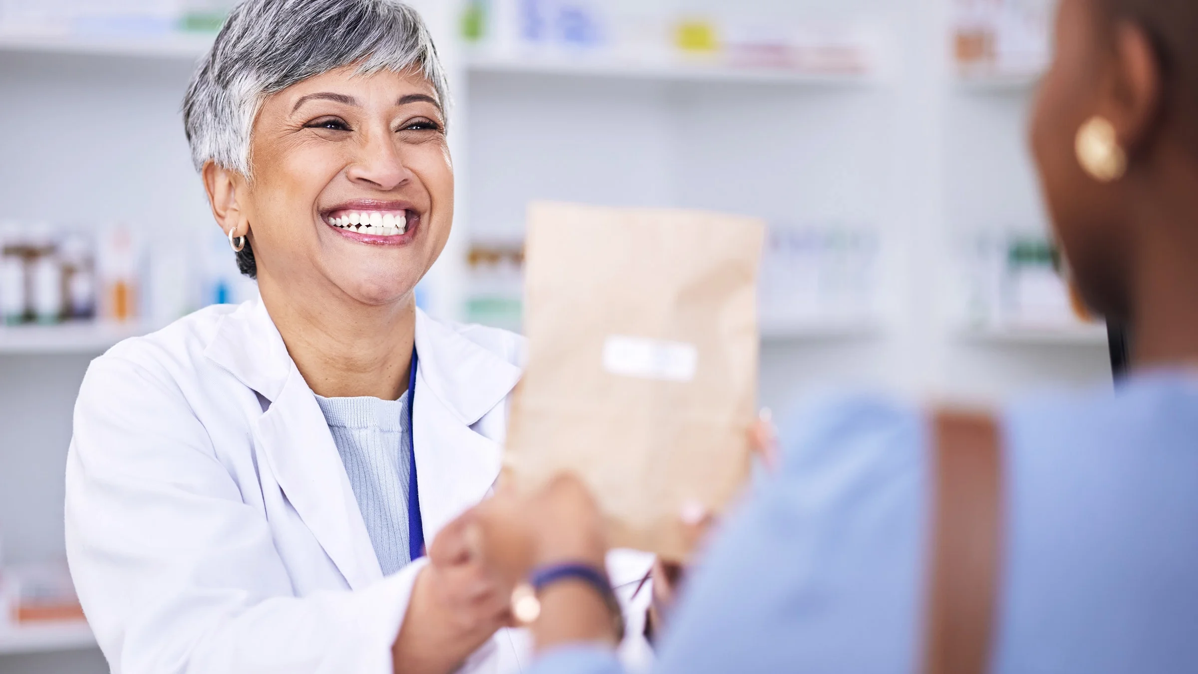 A pharmacist handing a paper bag to a patient.