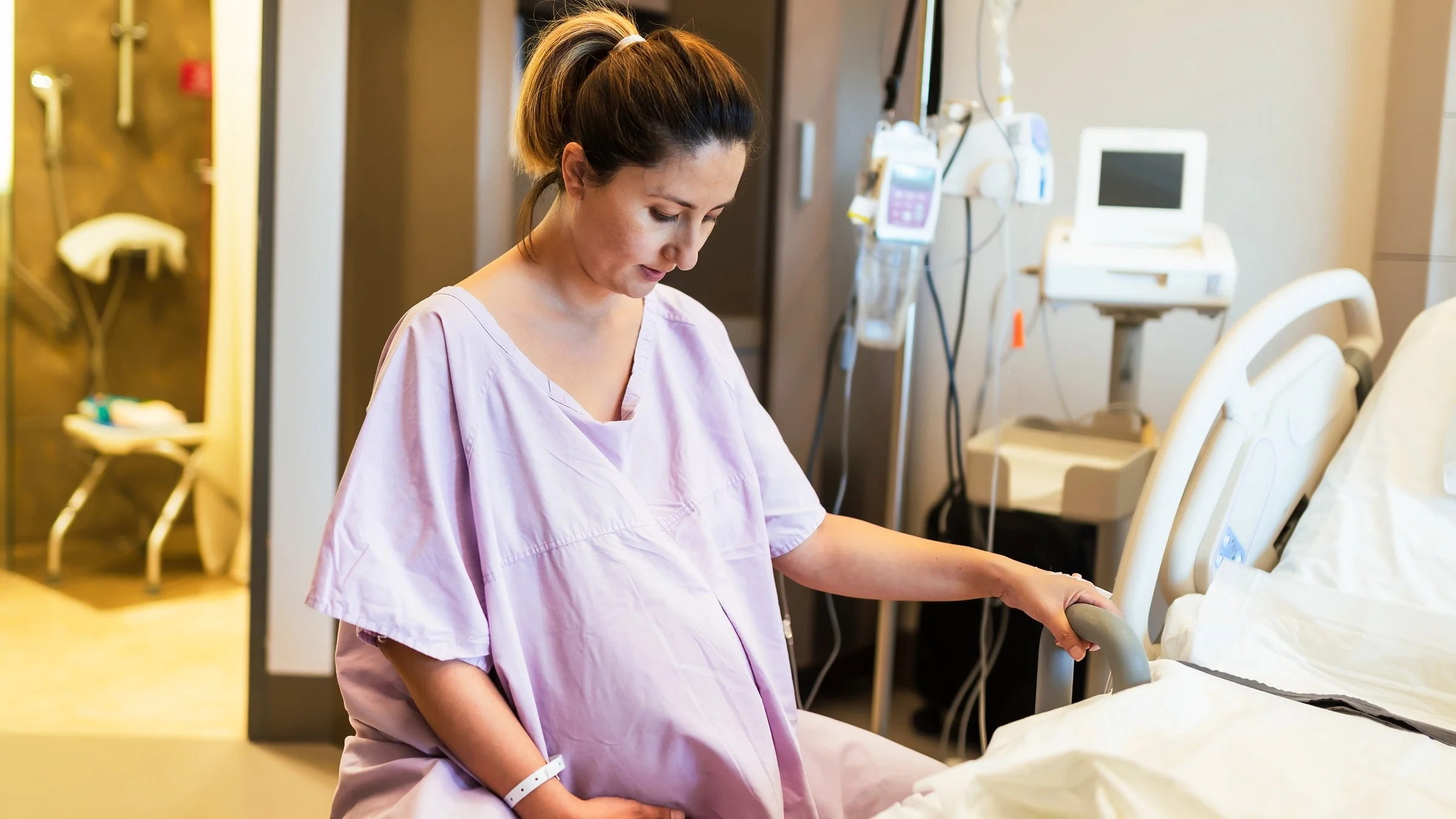 Young pregnant woman sitting on a yoga ball in the hospital delivery room. She is wearing a light pink hospital gown.