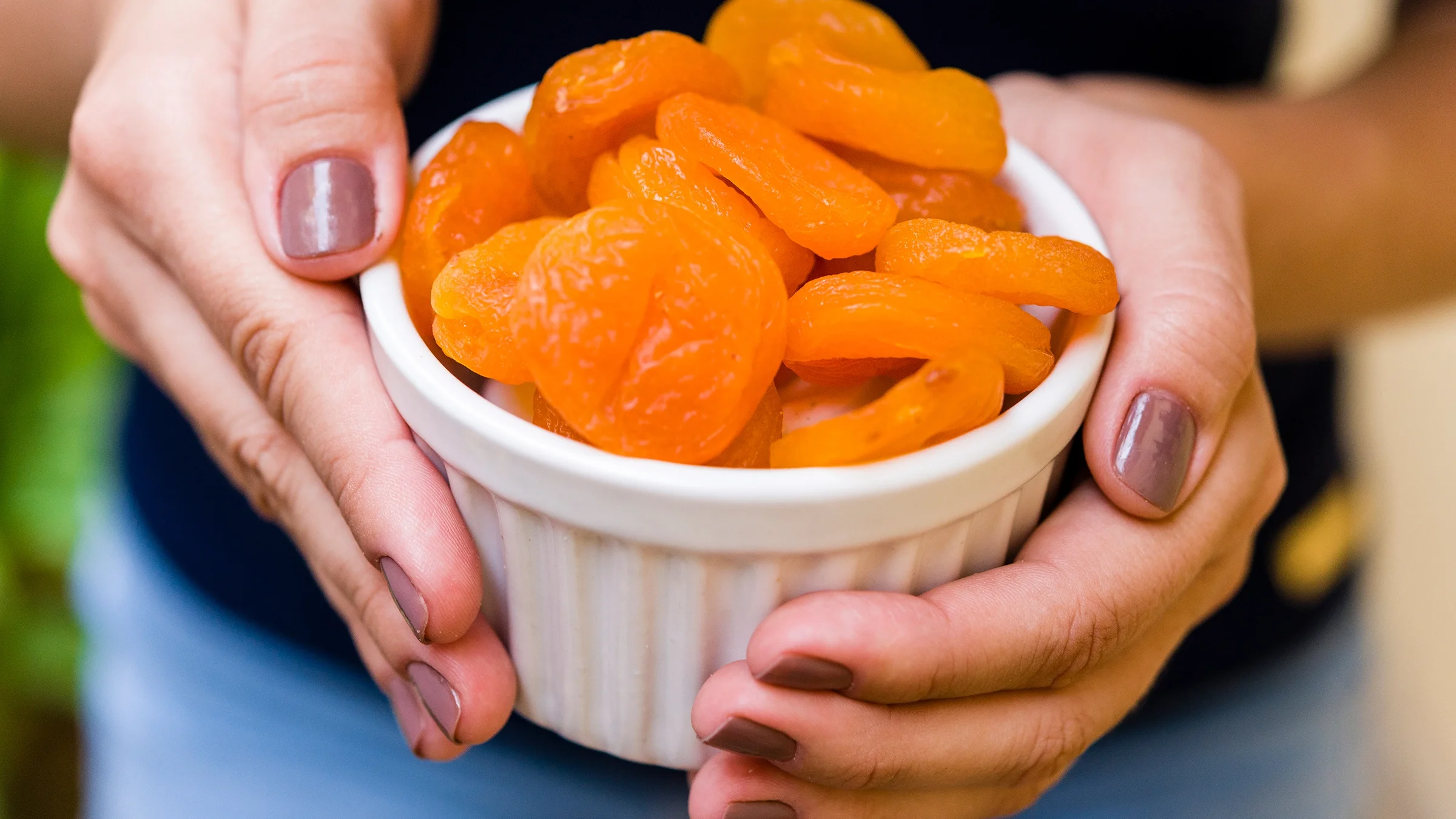 Close-up hands holding bowl of dried apricots.